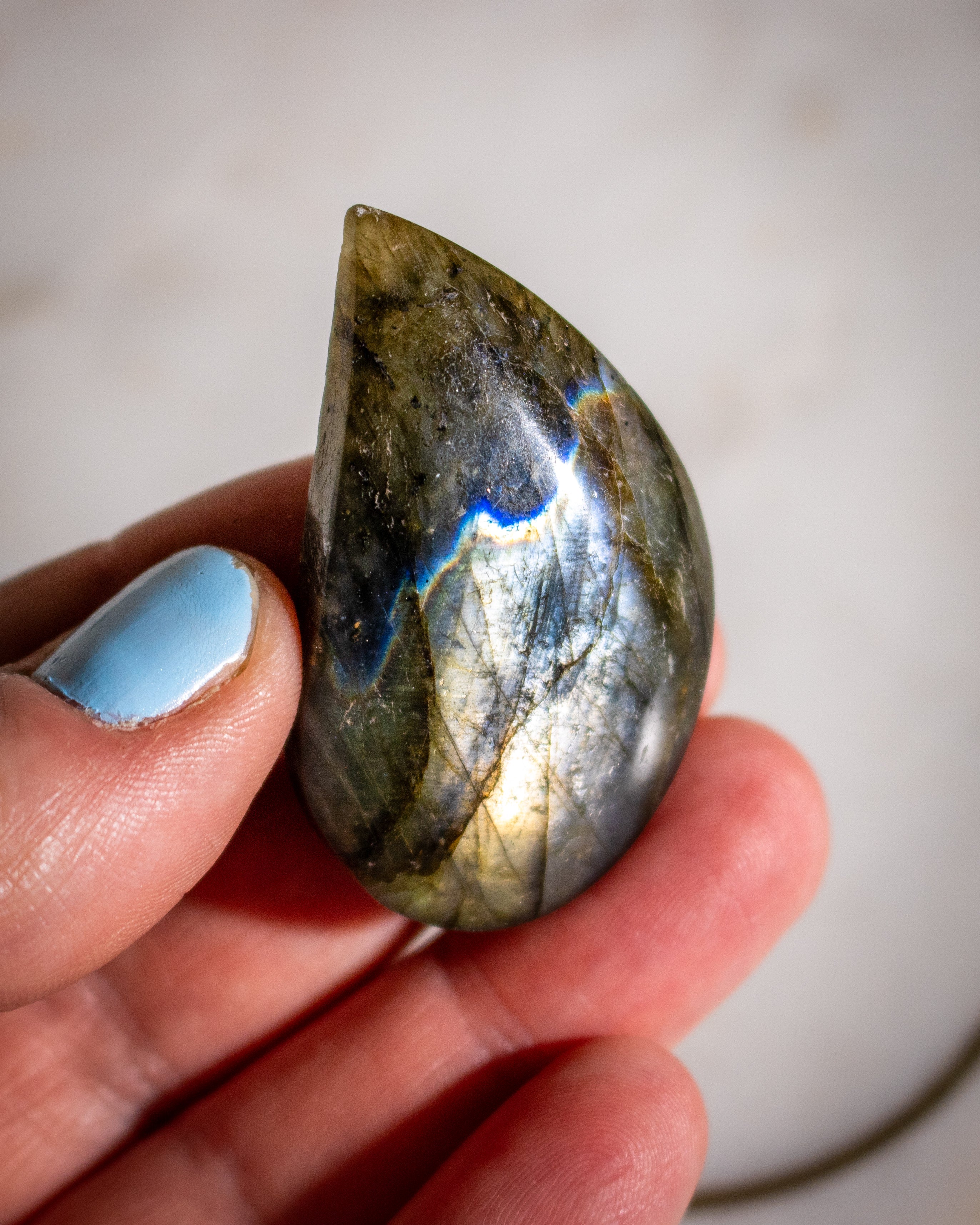 Hand holding a teardrop-shaped labradorite stone with a reflective surface.