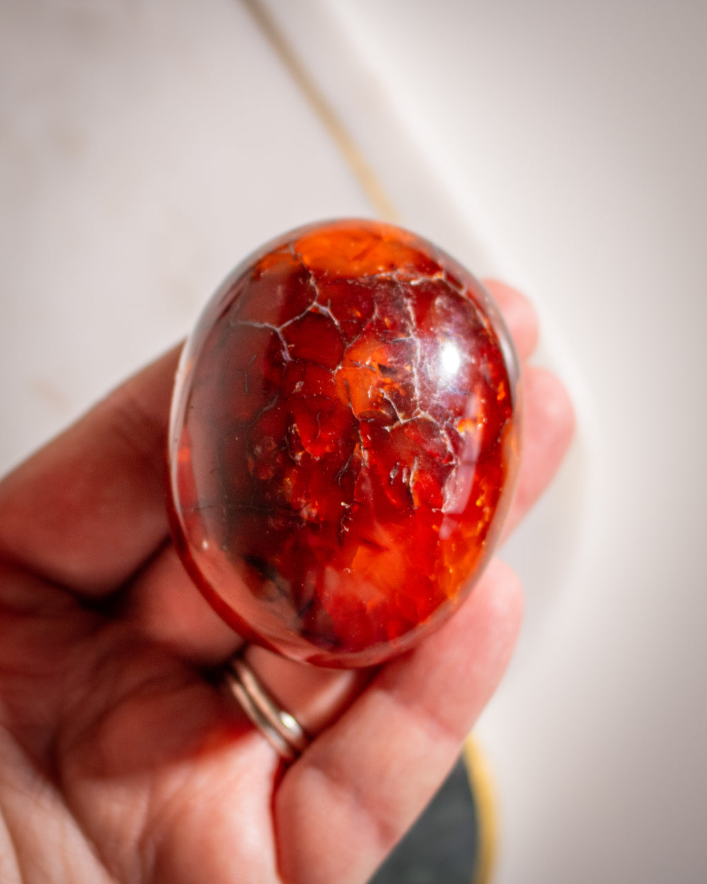 Hand holding a polished carnelian stone with visible cracks against a neutral background