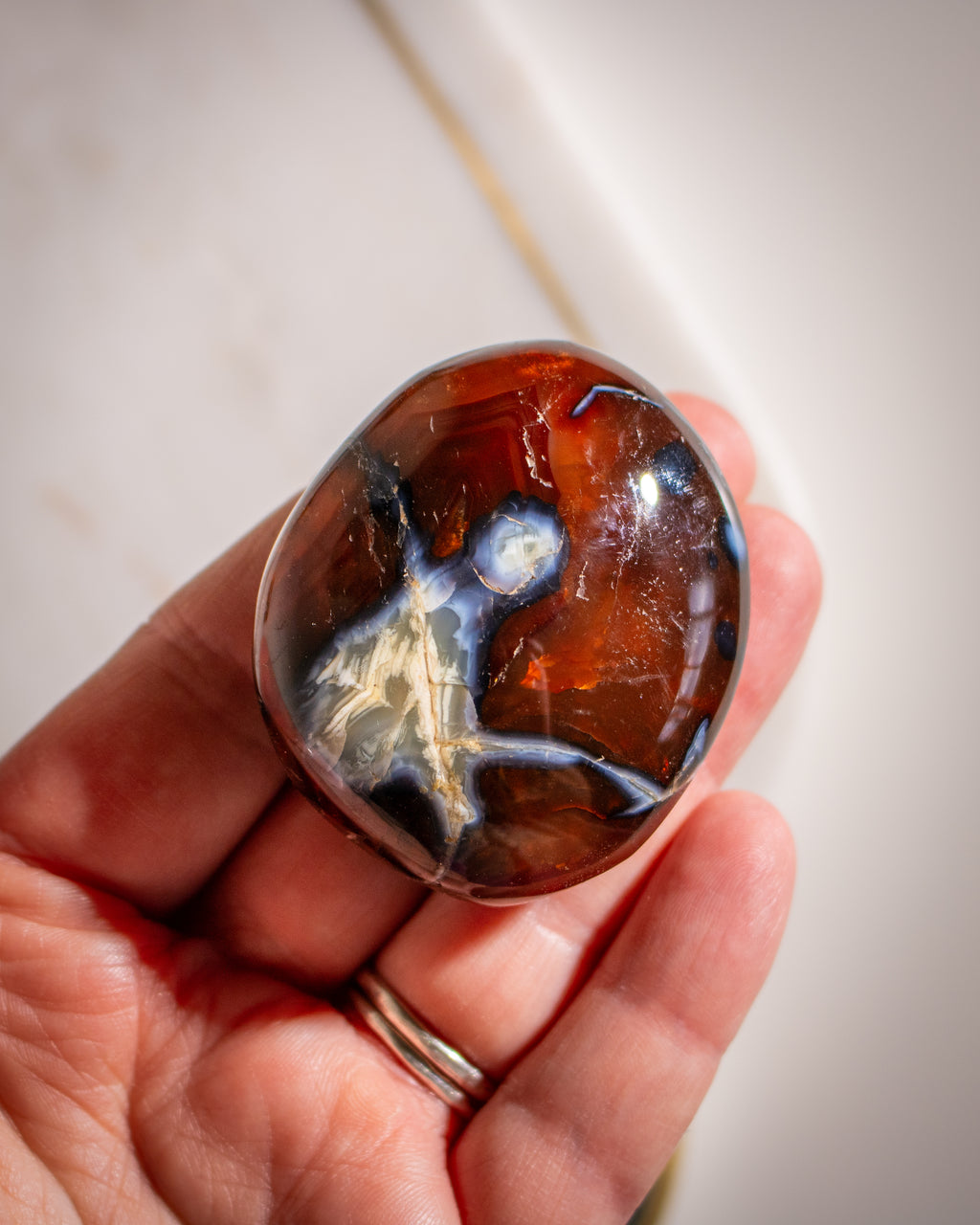 Hand holding a polished carnelian stone on a neutral background