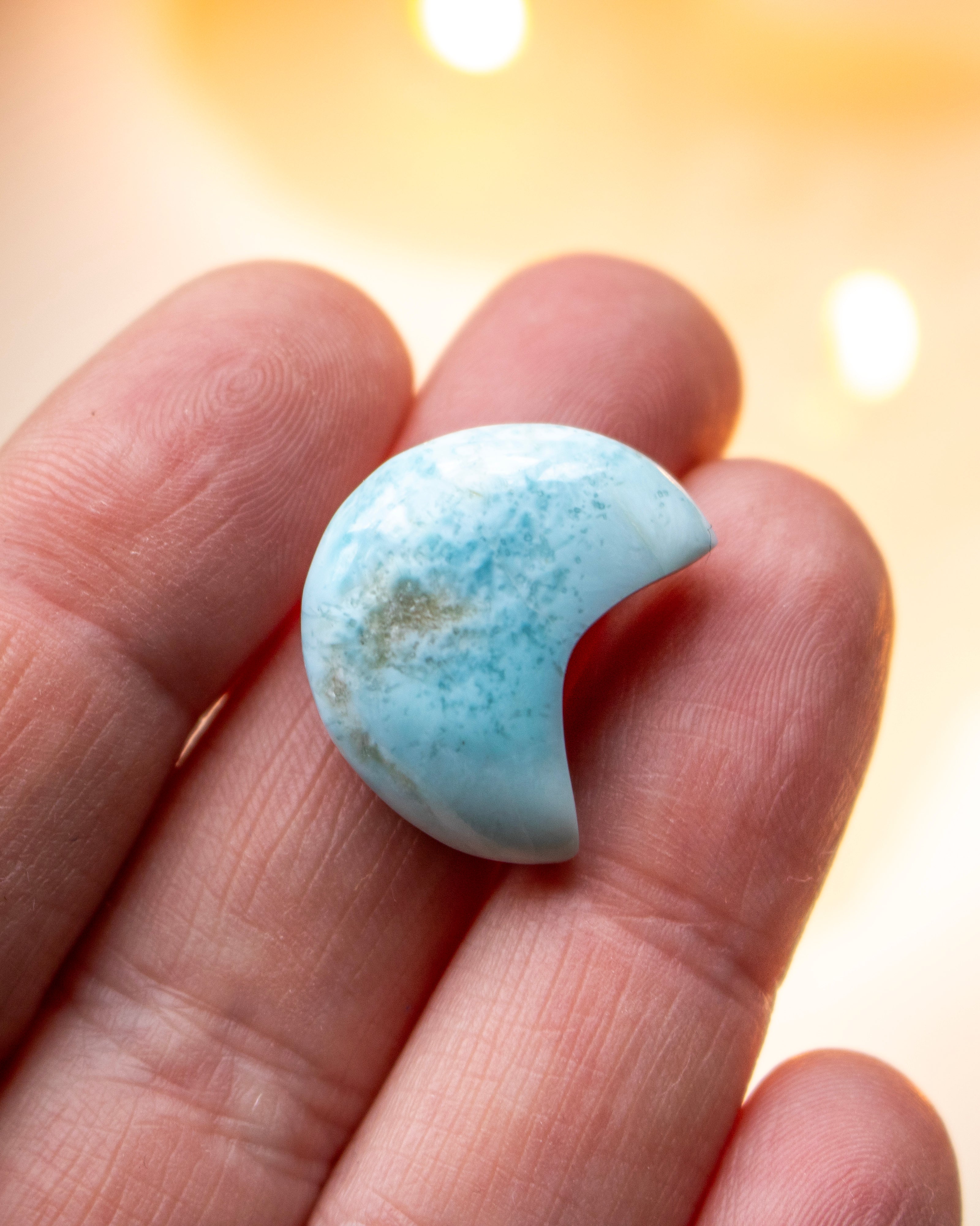 a small blue crescent shape stone resting on fingers of a hand