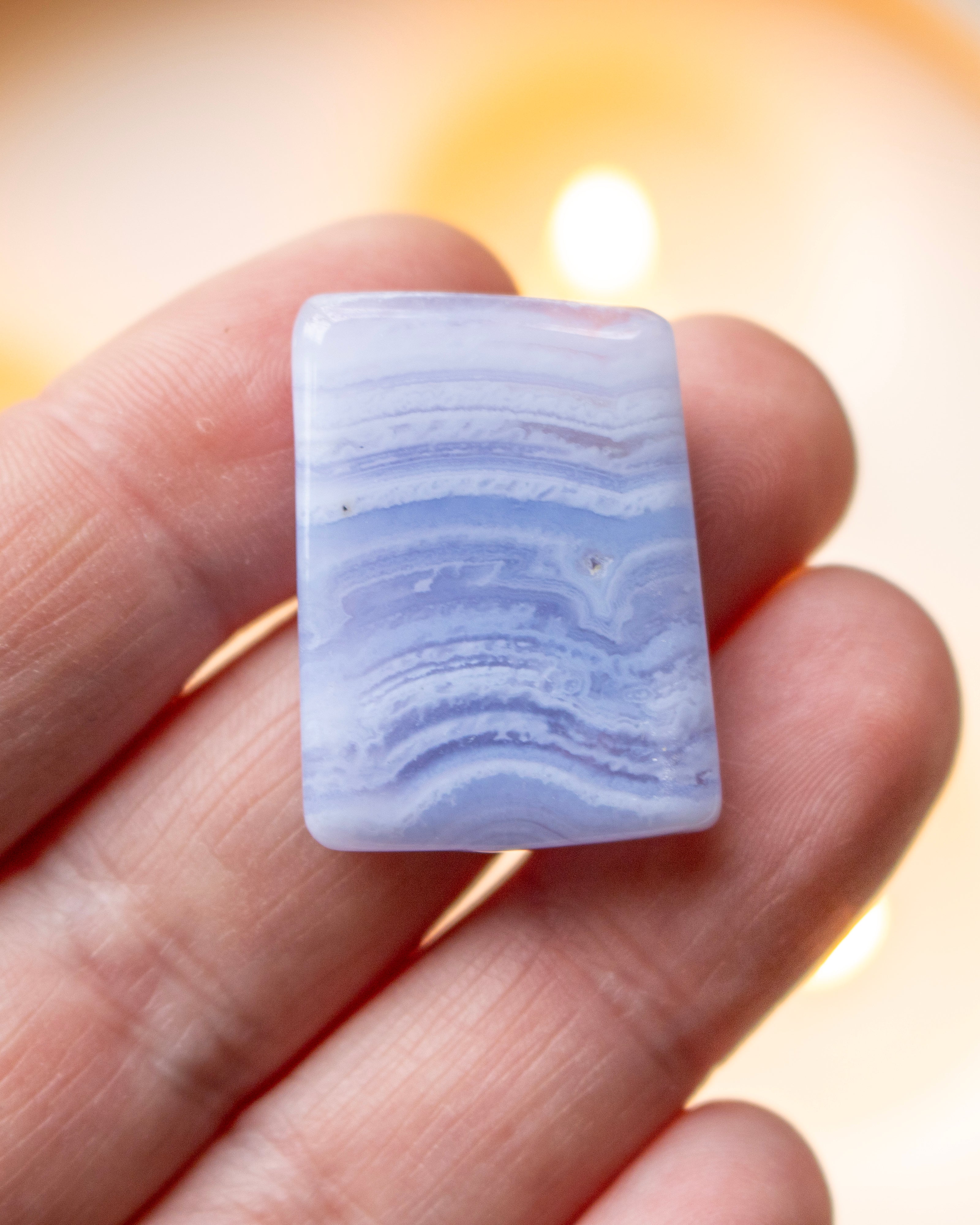 Rectangular blue lace agate stone held between fingers with a blurred background