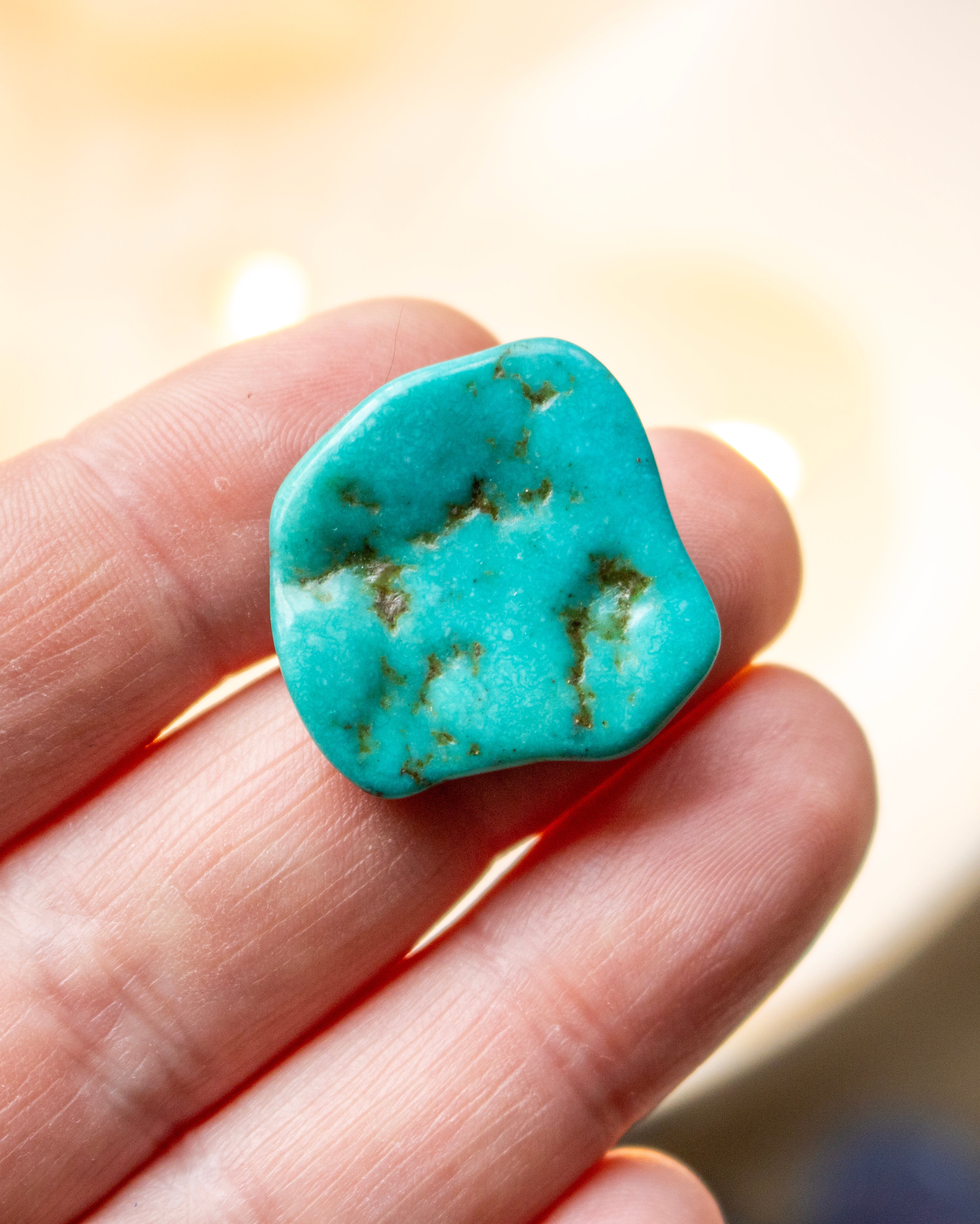 Turquoise stone held between fingers against a blurred background