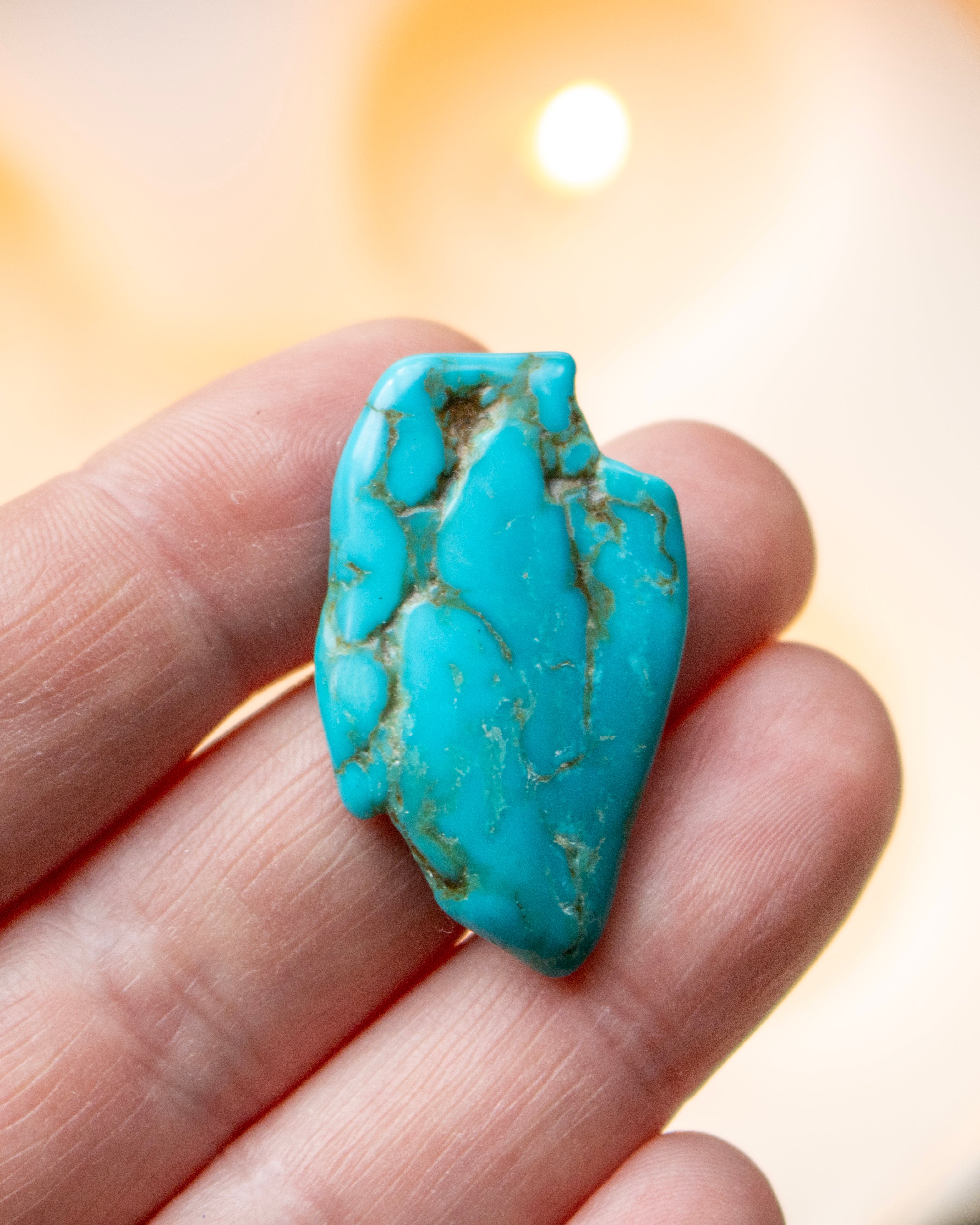 Turquoise stone held between fingers with a blurred background