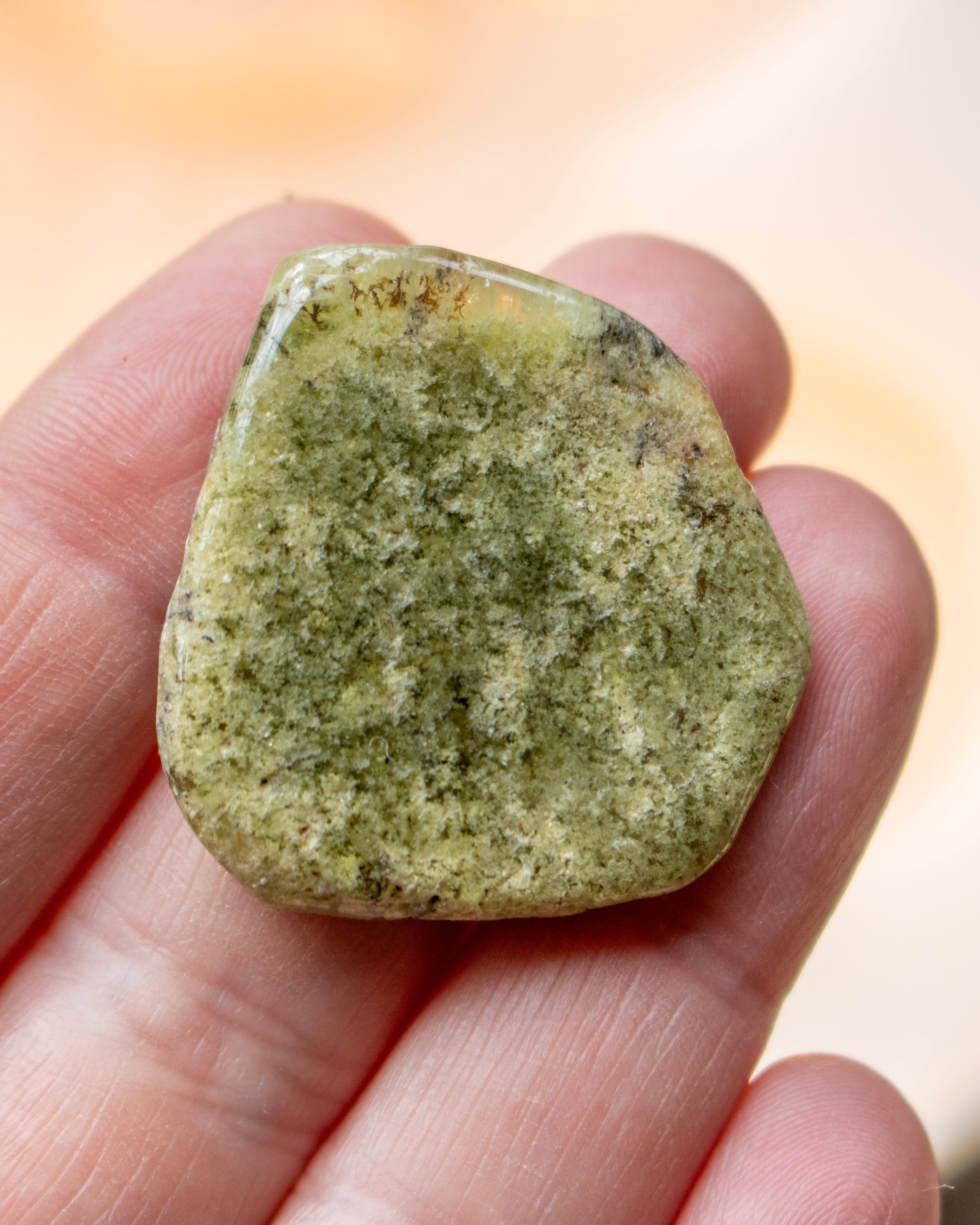 Hand holding a greenish stone against a blurred background