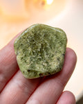 Green stone held in a hand with a blurred background