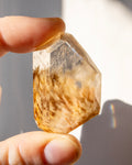 Hand holding a quartz crystal against a neutral background
