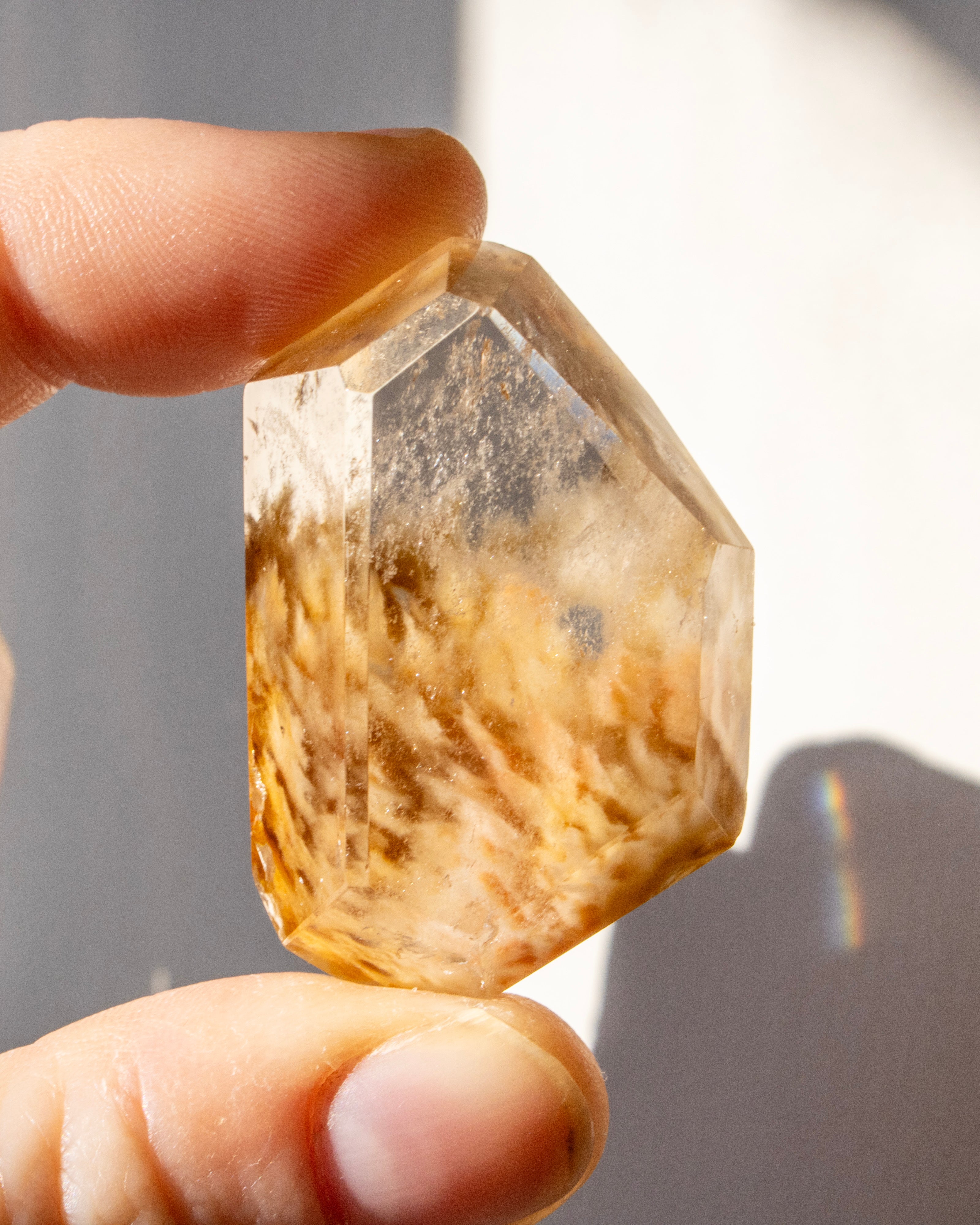 Hand holding a quartz crystal against a neutral background