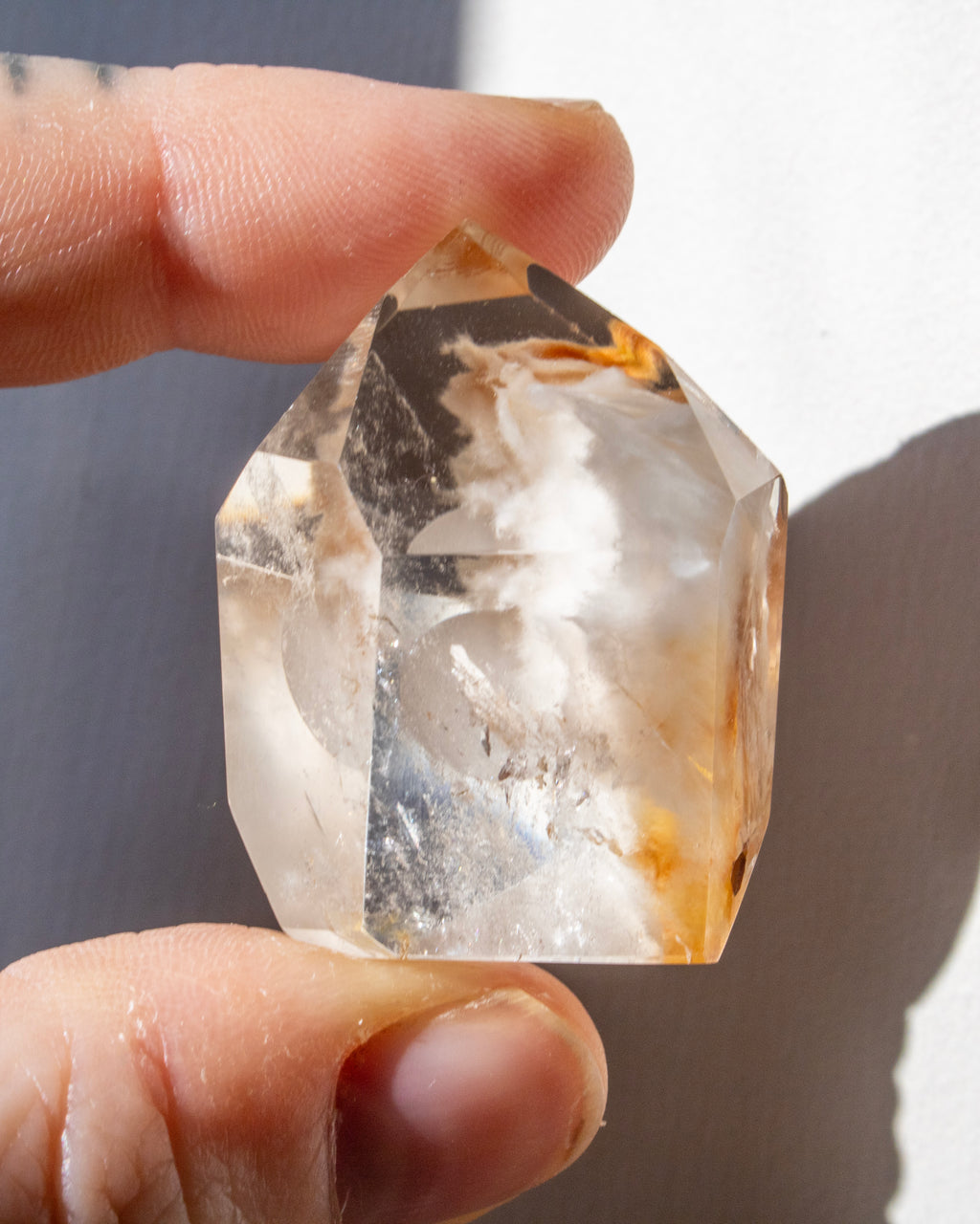 Hand holding a clear crystal with visible inclusions against a neutral background