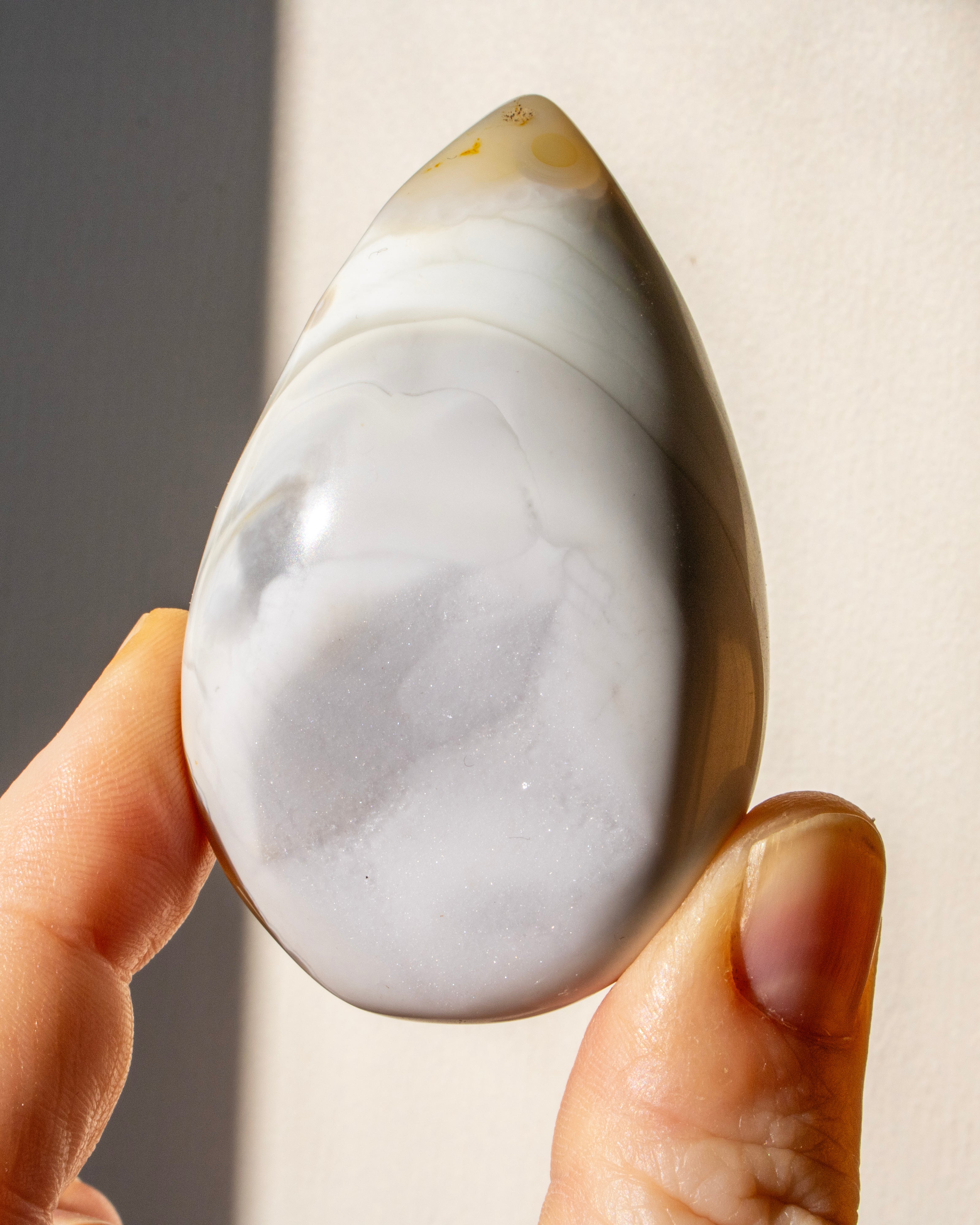 a hand holding a teardrop shaped beige stone