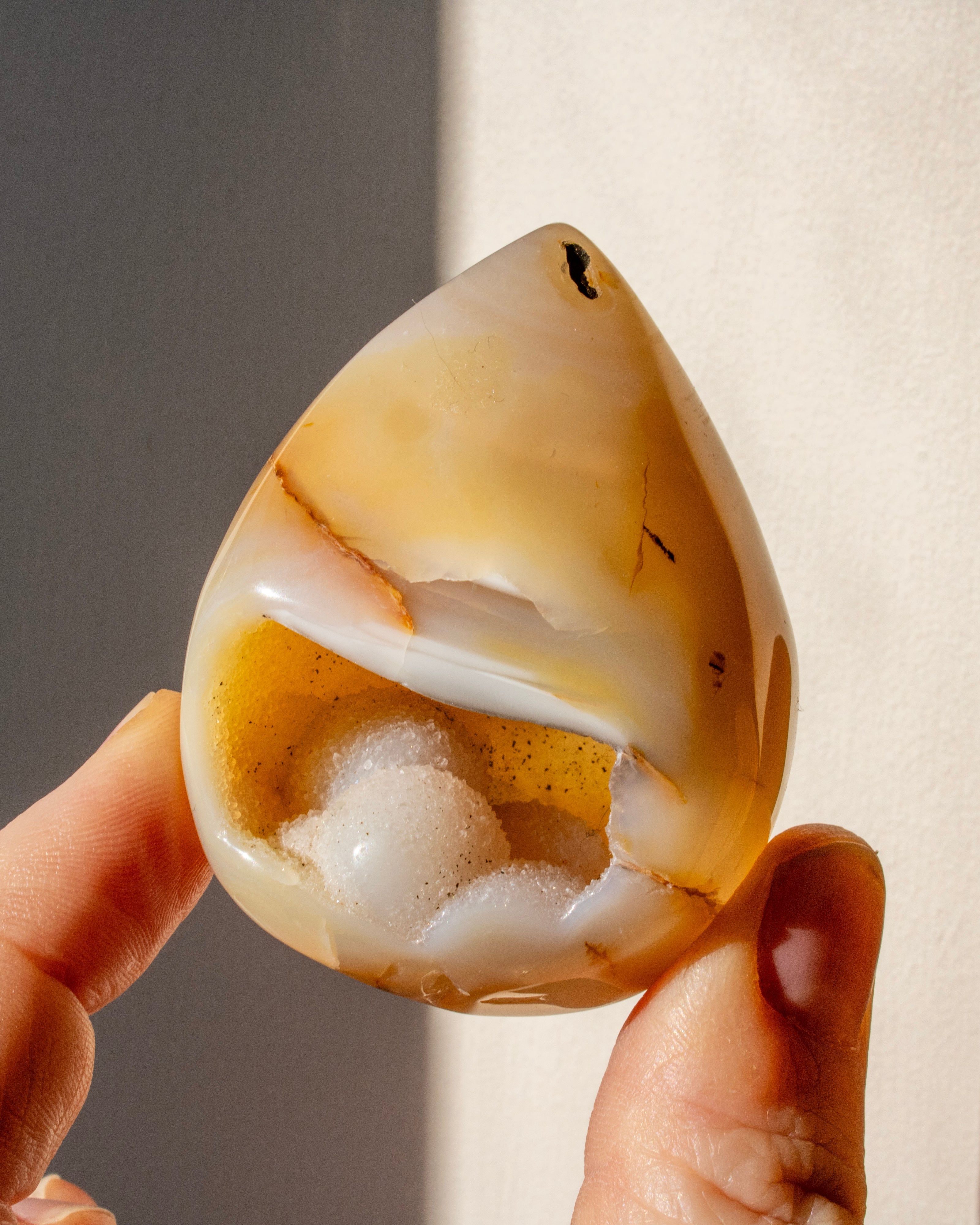 a hand holding a teardrop shape beige geode crystal