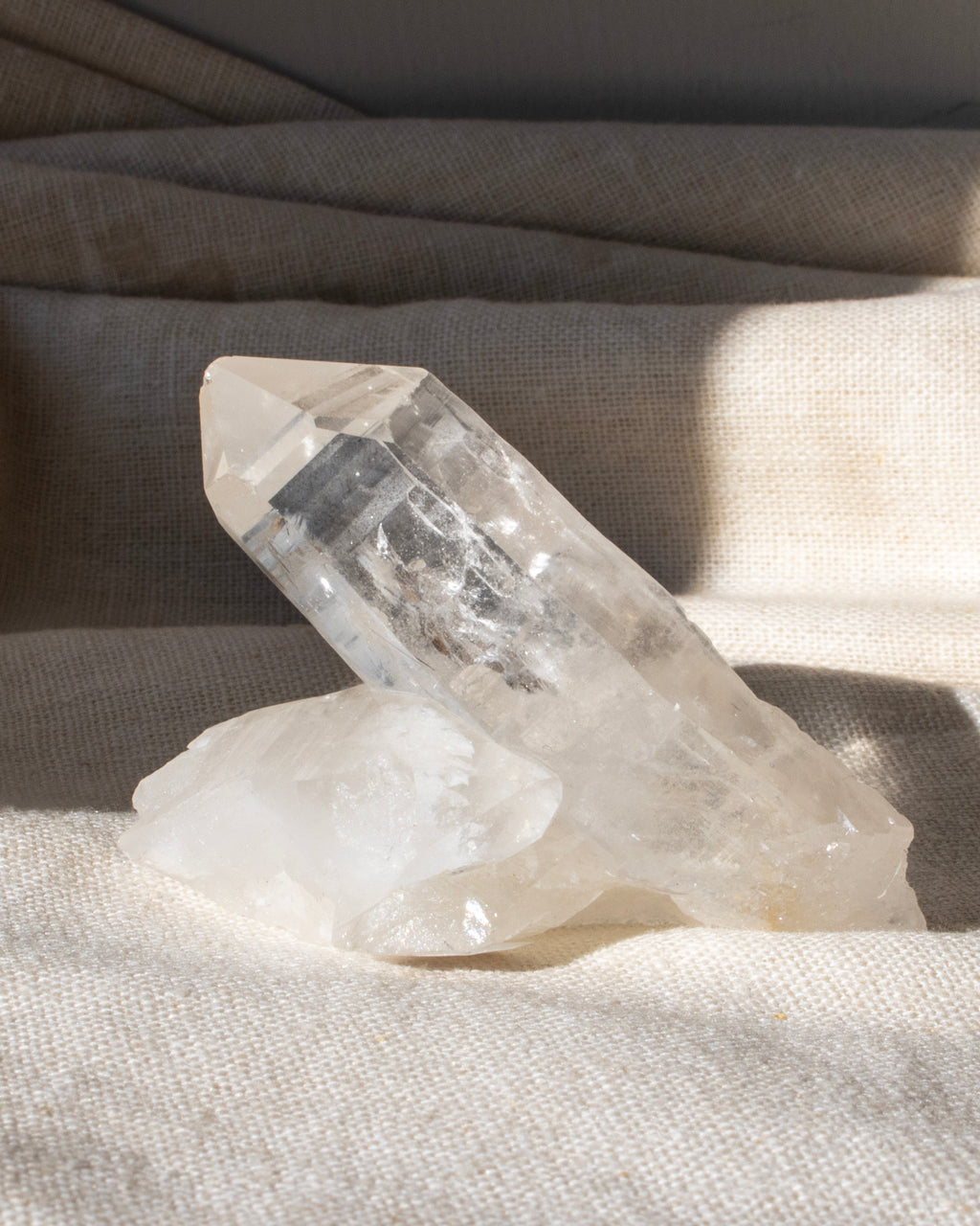 a clear quartz cluster sitting on a textured beige fabric