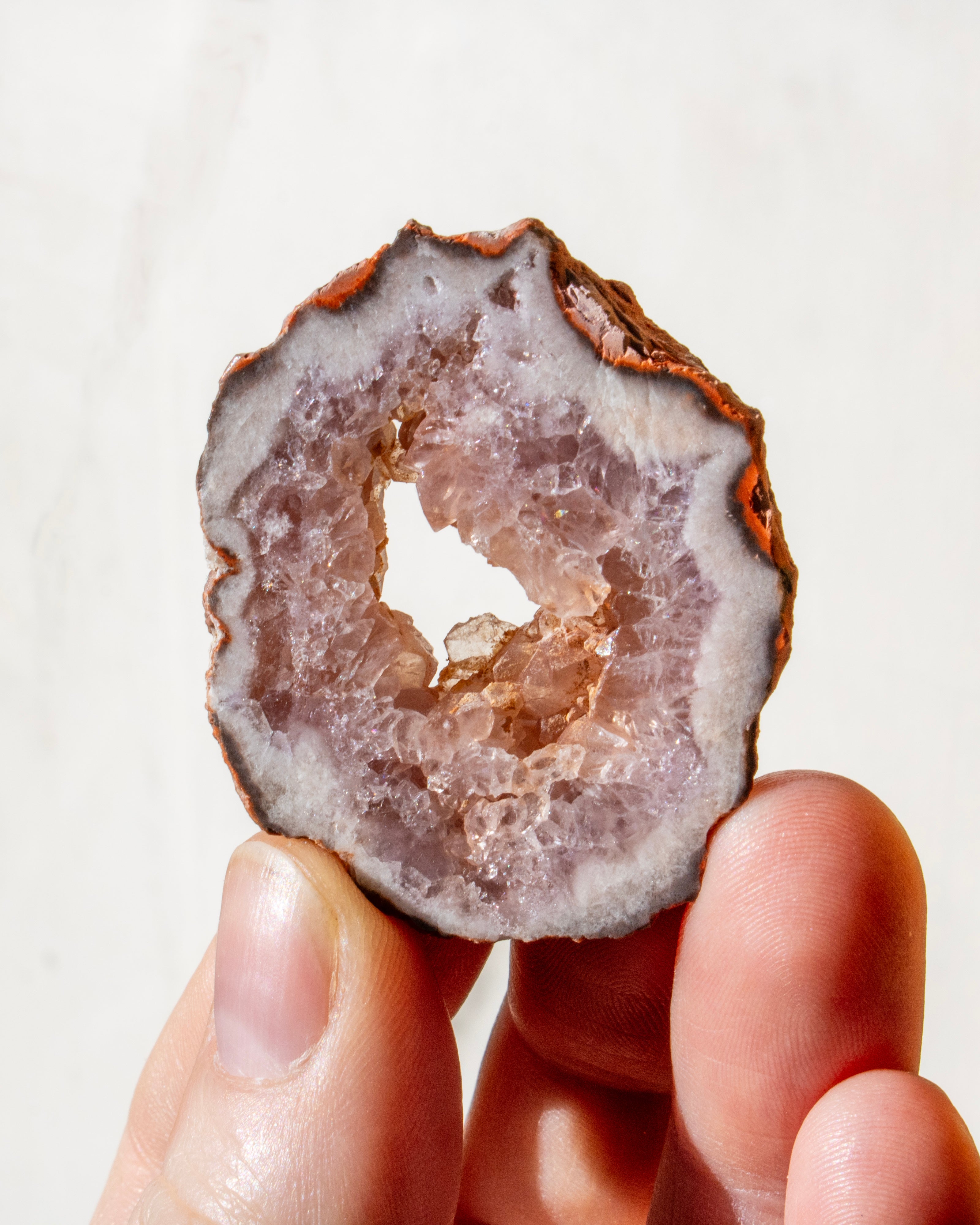 hand holding a pink geode crystal with a hole through the middle