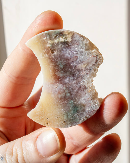 hand holding a multi-coloured moon shaped stone
