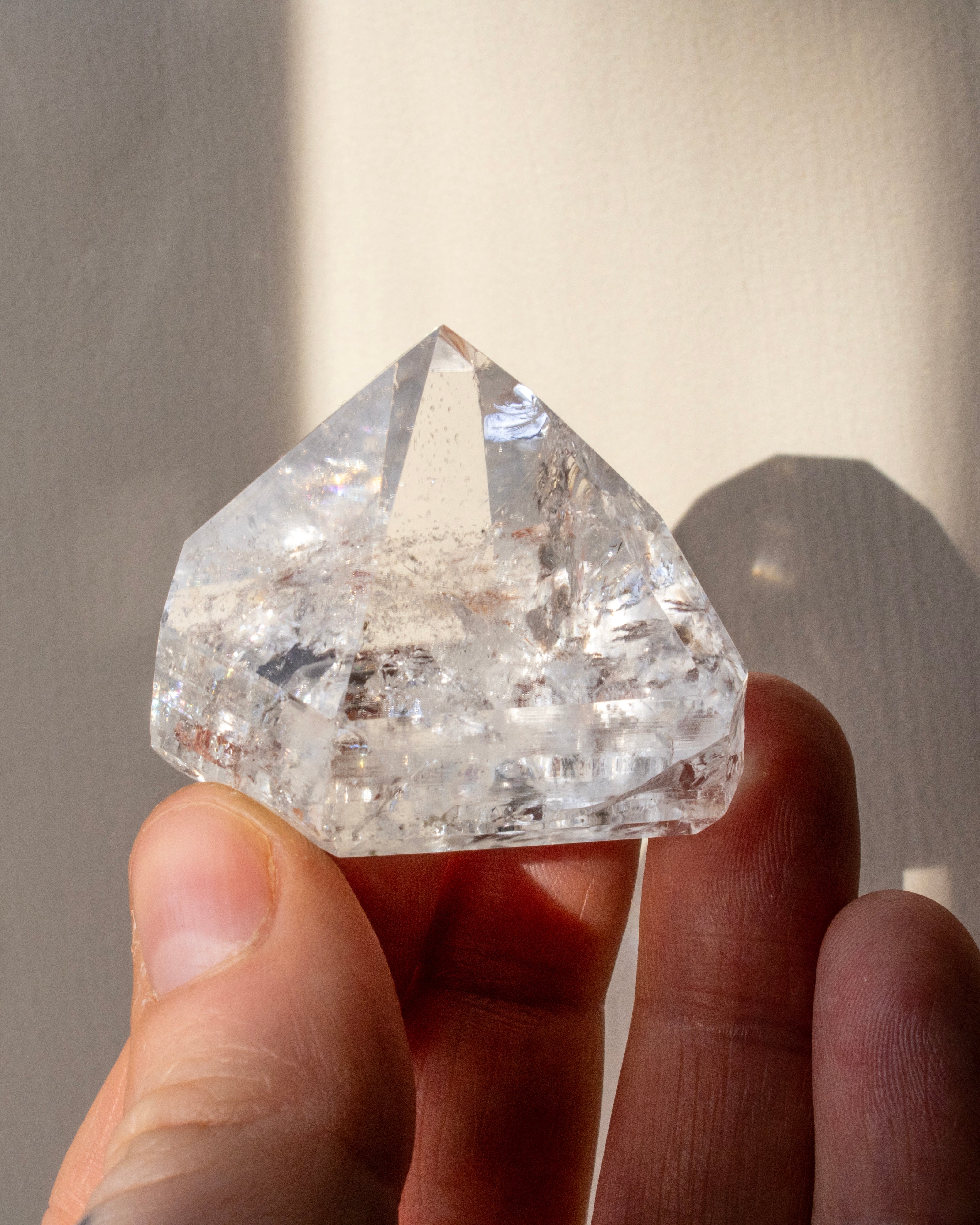 Clear quartz held between fingers against a neutral background