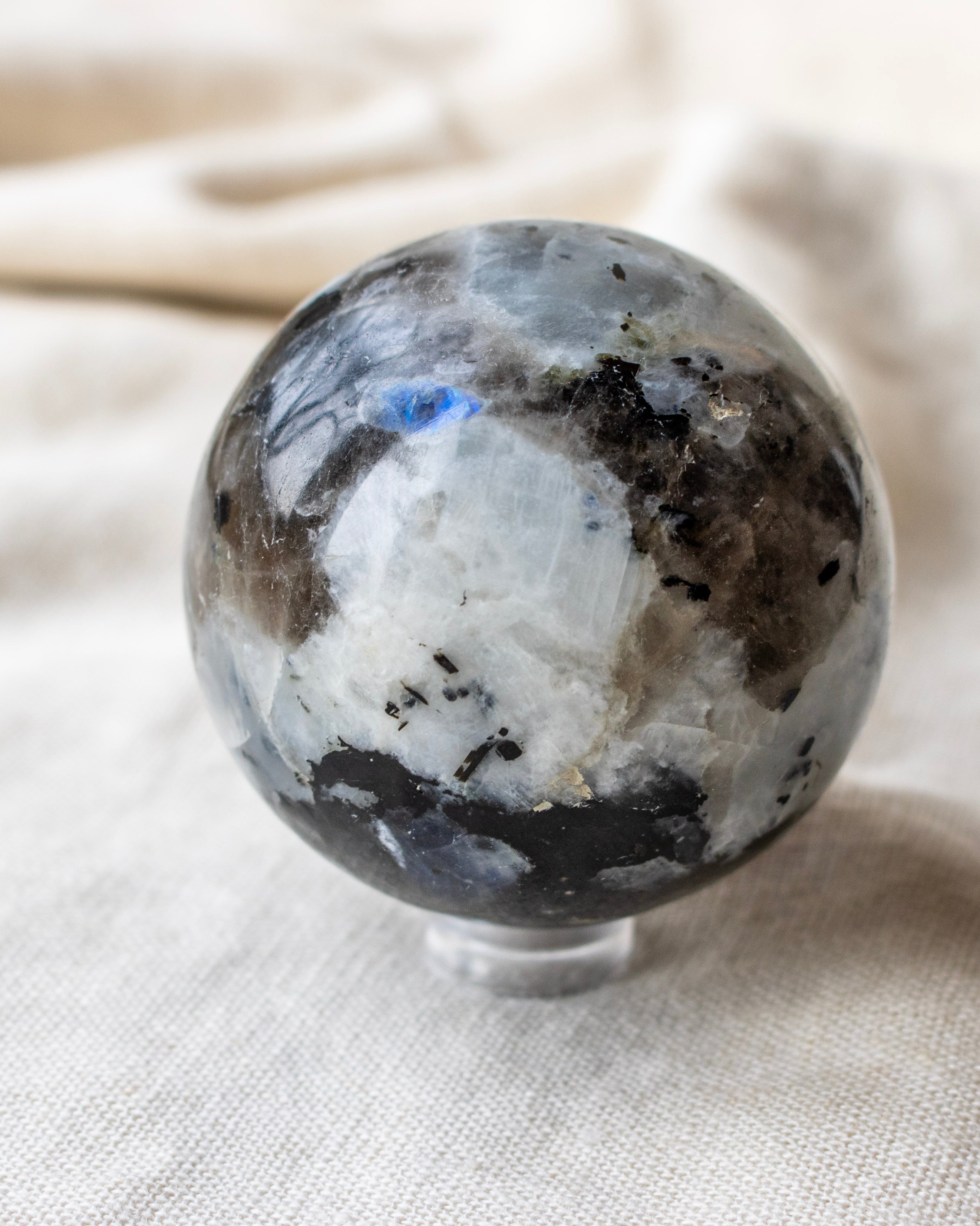 a white and black stone ball with a bright blue patch sitting on a beige linen textured fabric 