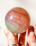 Hand holding a rainbow-colored crystal ball against a white background