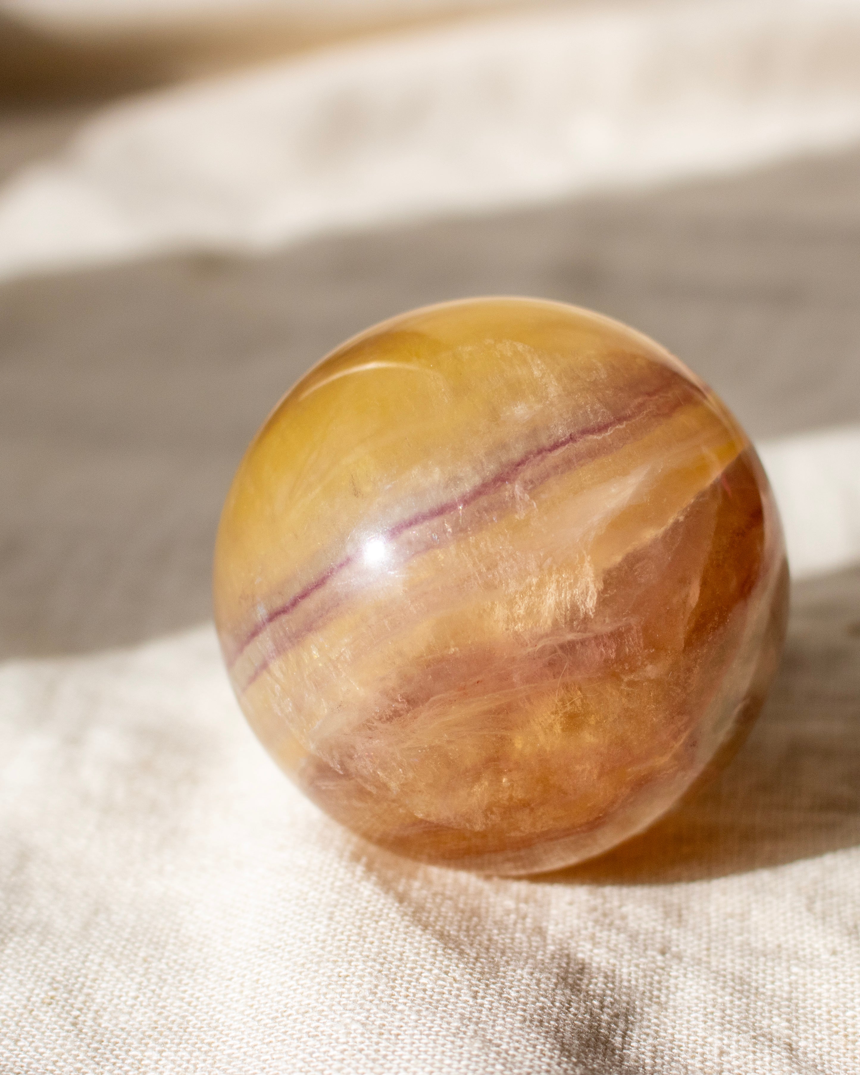 yellow crystal sphere with purple bands on a fabric linen background