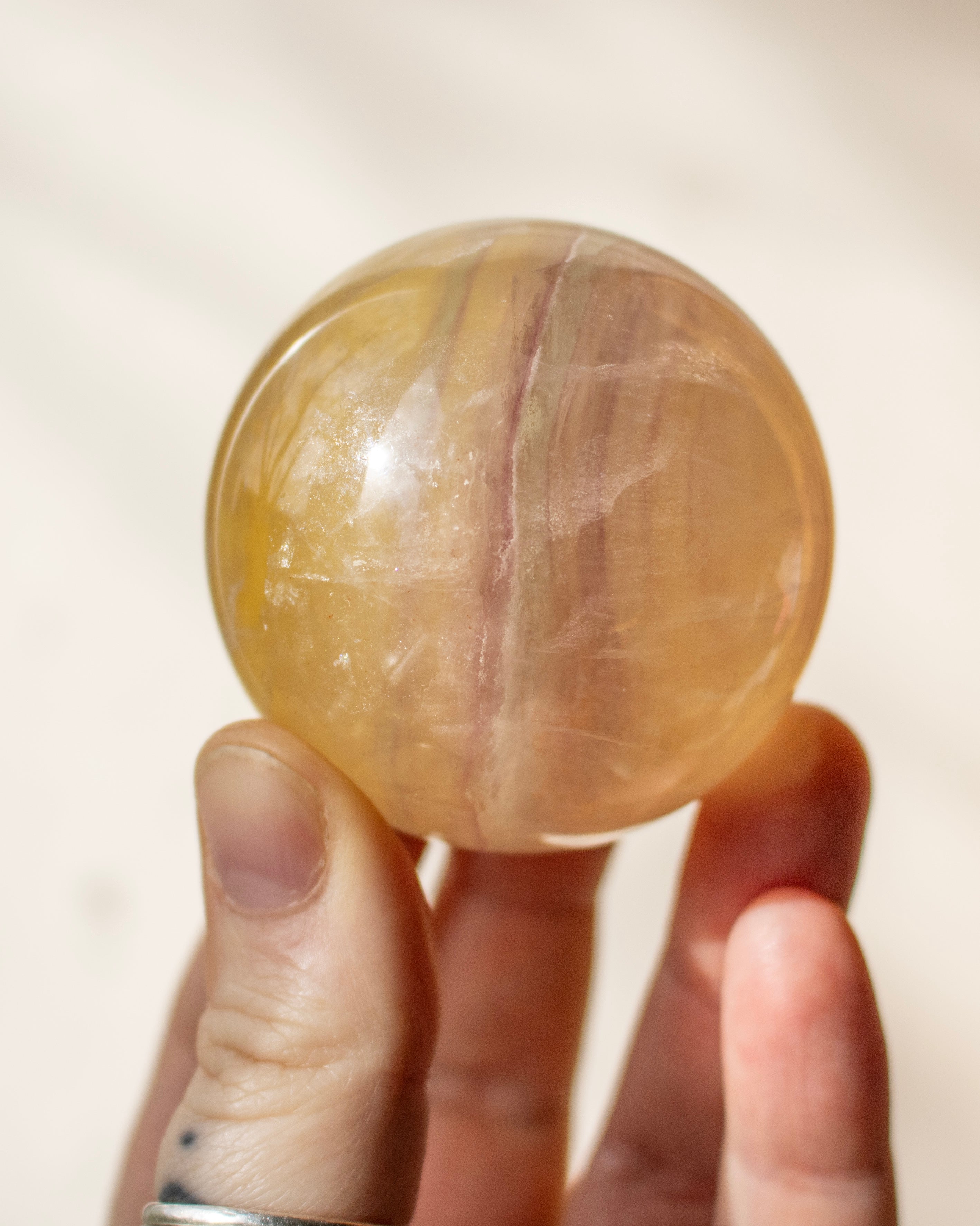 a yellow fluorite sphere with purple bands being held in a hand