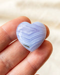 a banded blue heart shaped stone held on fingers