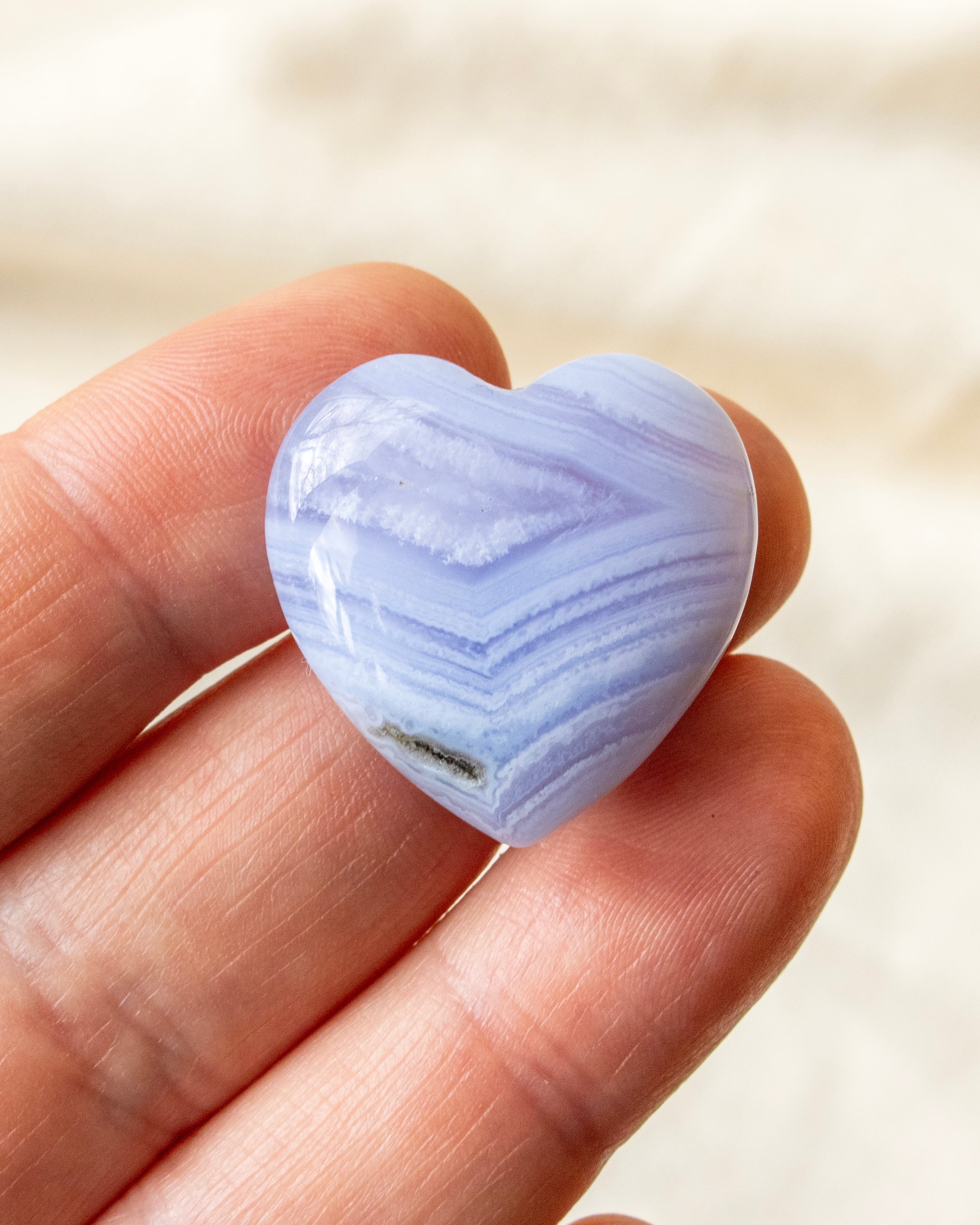 a banded blue heart shaped stone held on fingers