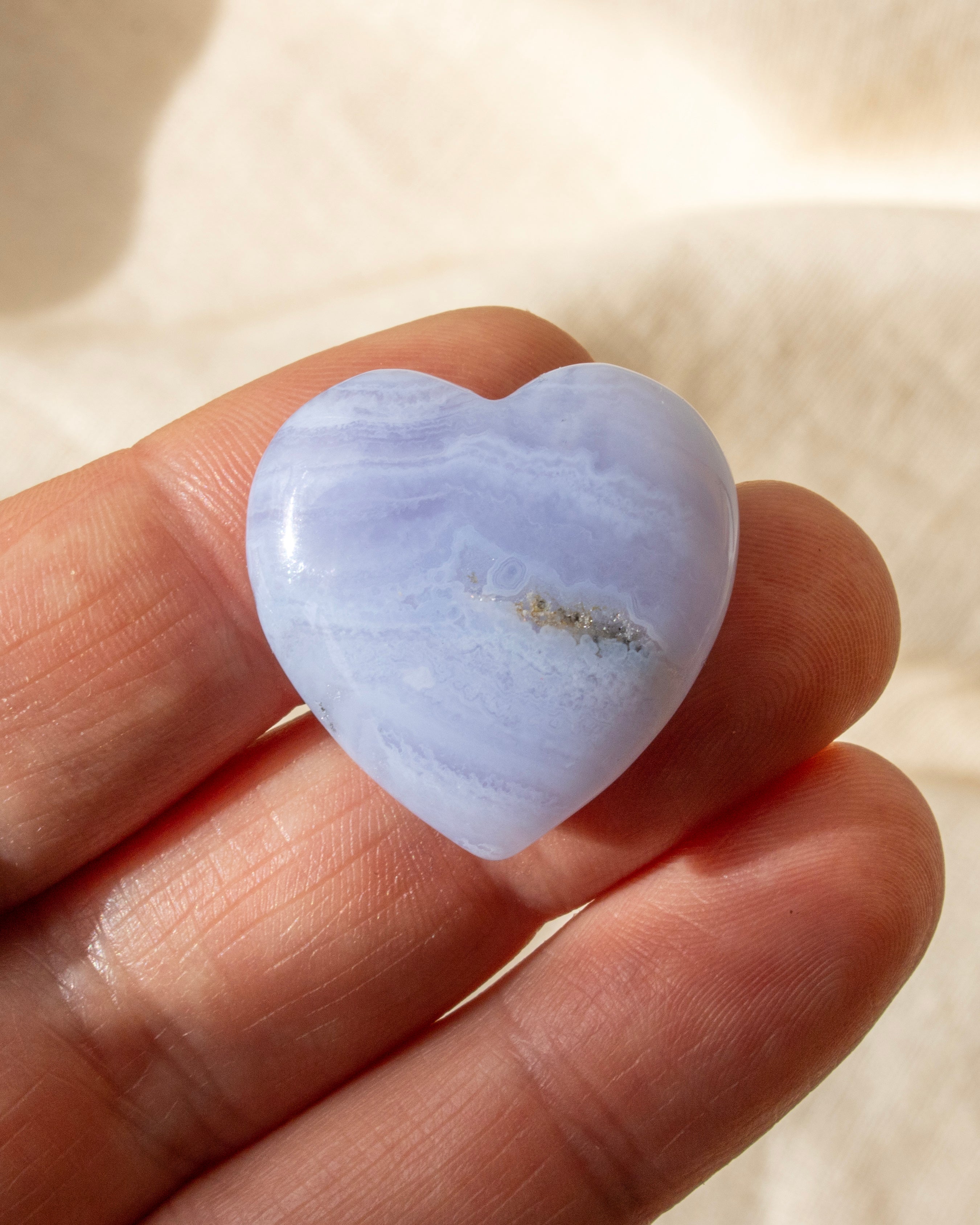 a banded blue heart shaped stone held on fingers