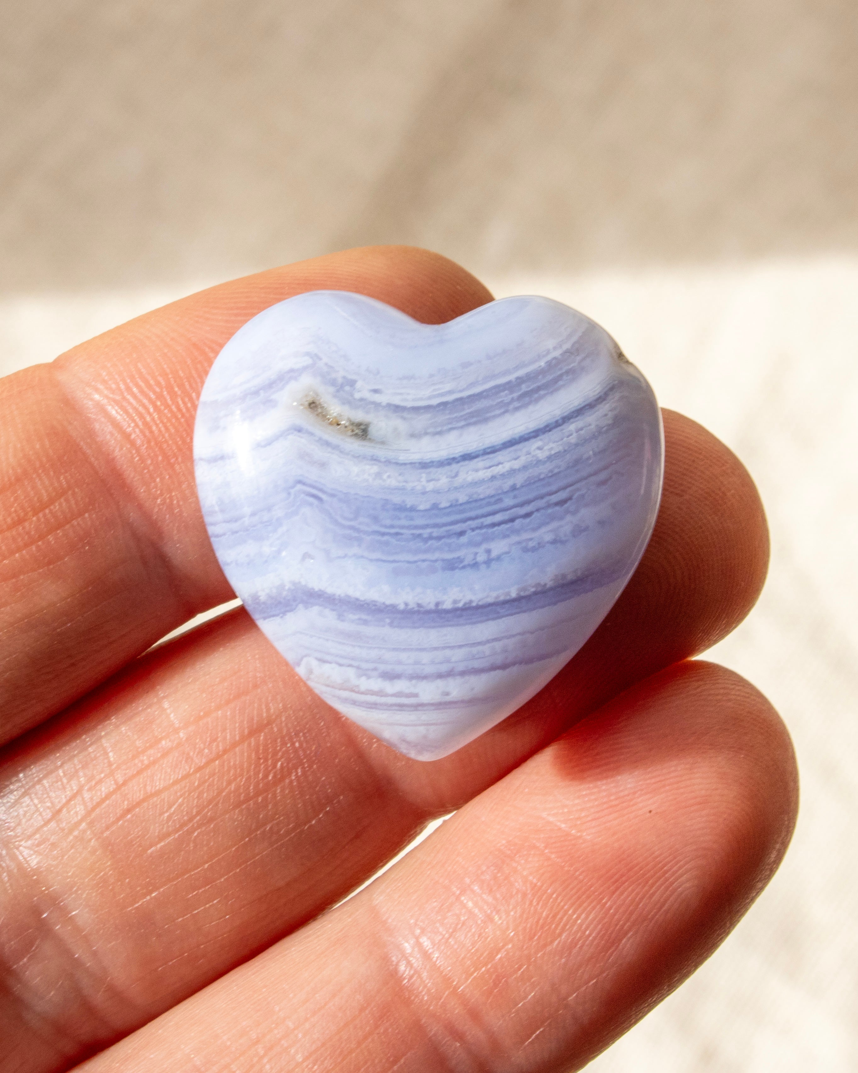 a banded blue heart shaped stone held on fingers