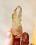 a yellowed quartz crystal point being held in fingers with a beige background
