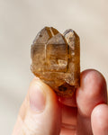 a yellowed quartz crystal point being held in fingers with a beige background