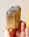 a yellowed quartz crystal point being held in fingers with a beige background