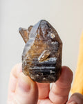 a yellowed quartz crystal point being held in fingers with a beige background