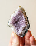 Amethyst crystal held in a hand against a neutral background