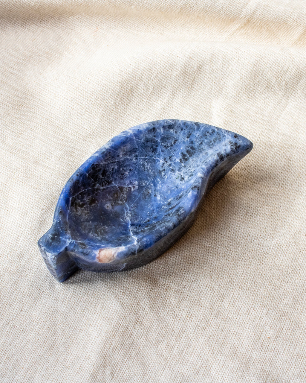 Blue stone leaf-shaped dish on a beige fabric background