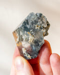 Hand holding a rough crystal rock against a neutral background