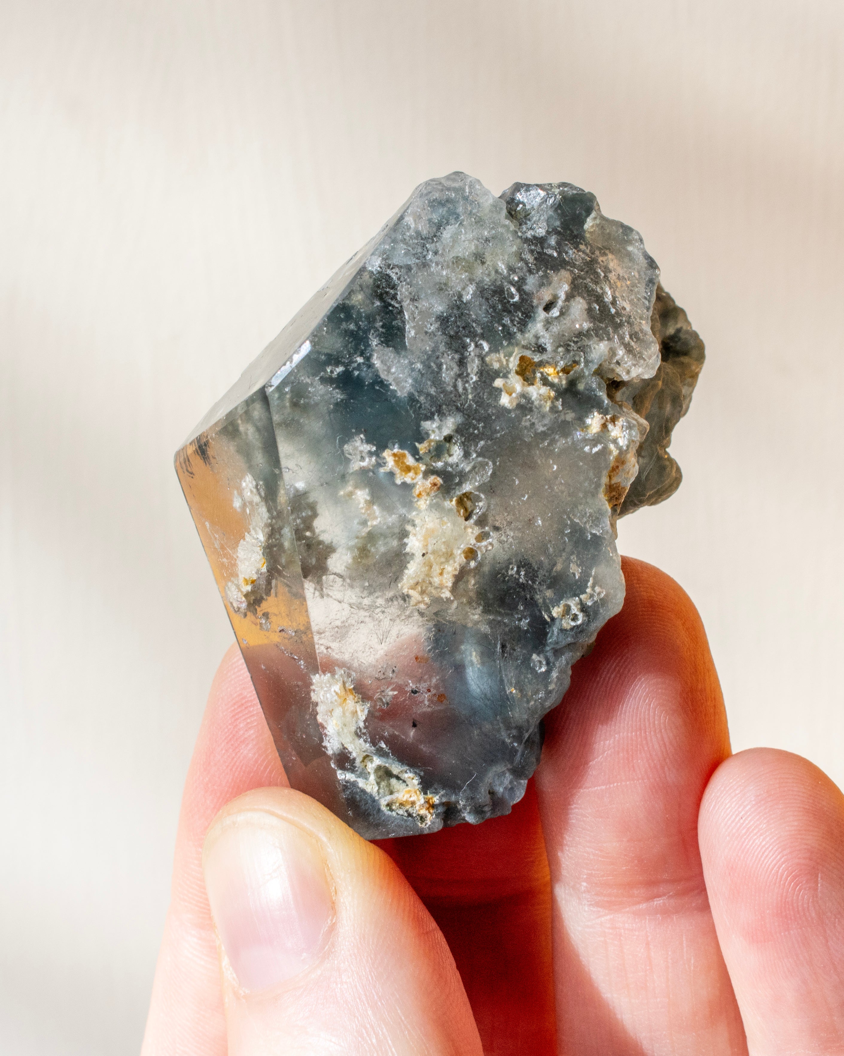 Hand holding a rough crystal rock against a neutral background