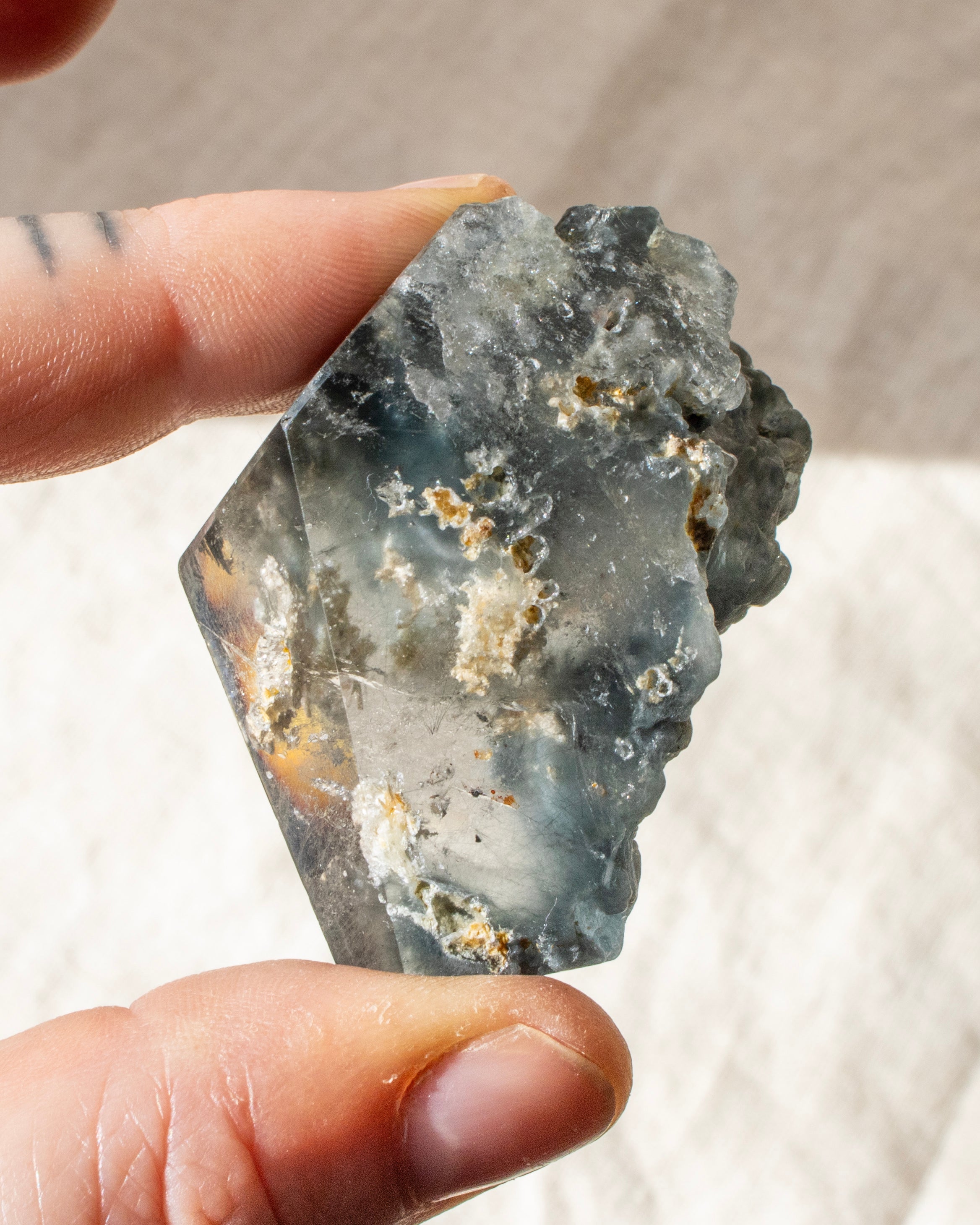 Crystal with a face-like carving held by a hand against a neutral background