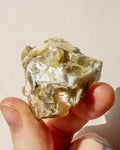 Hand holding a rough crystal rock against a neutral background
