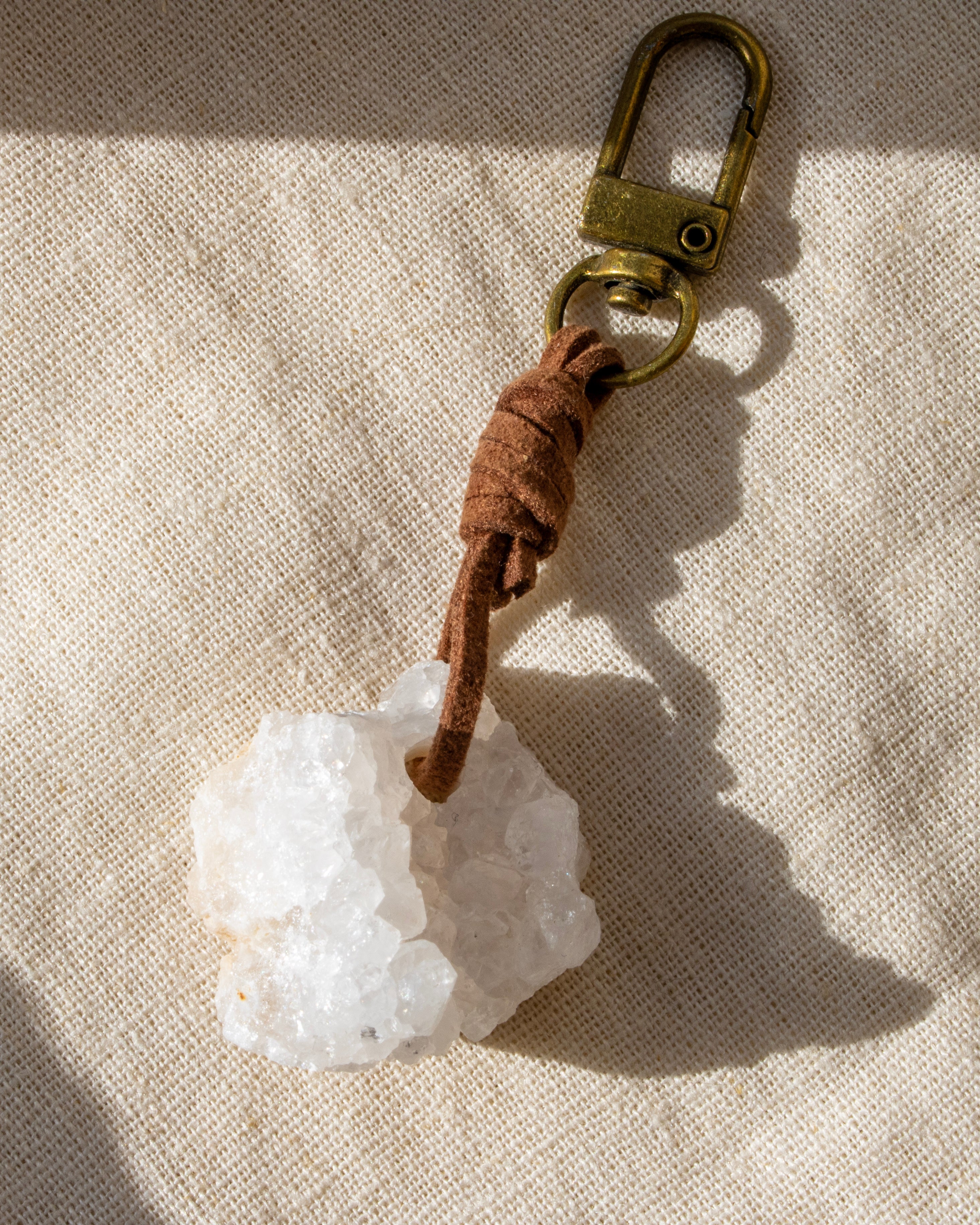Keychain with a white stone and brown leather strap on a beige fabric background