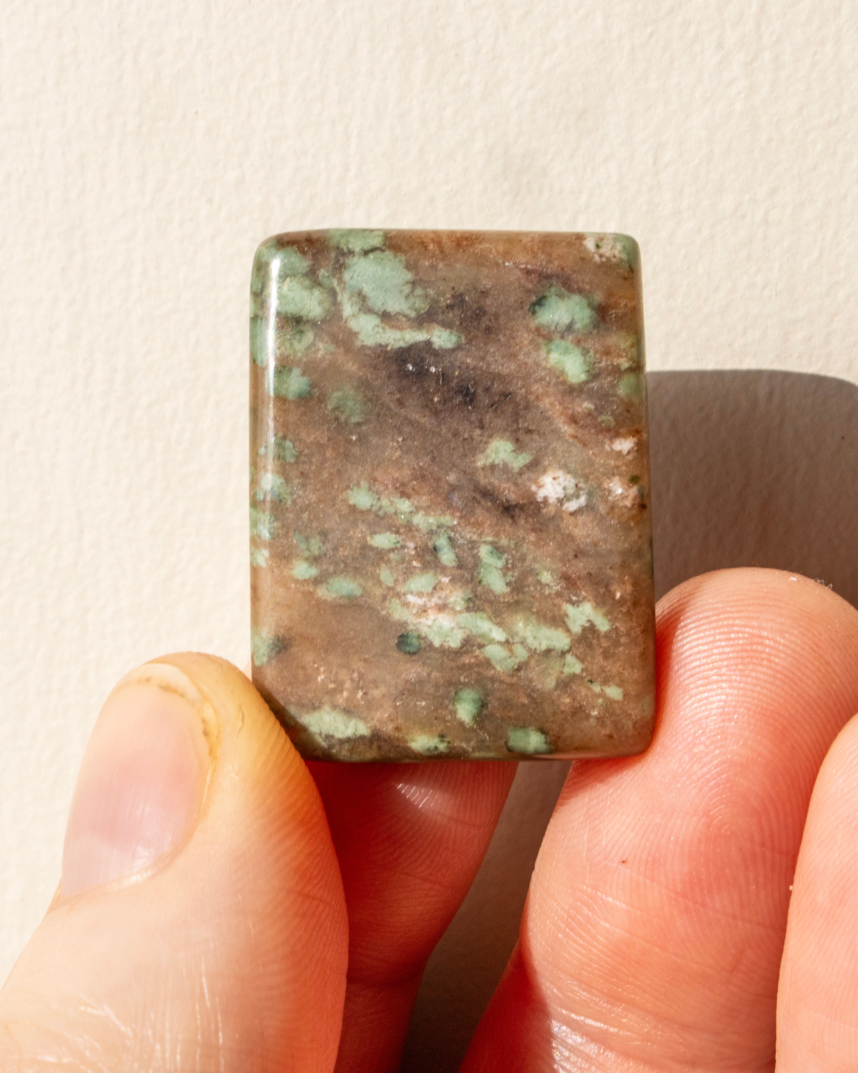 Rectangular stone held between fingers against a neutral background