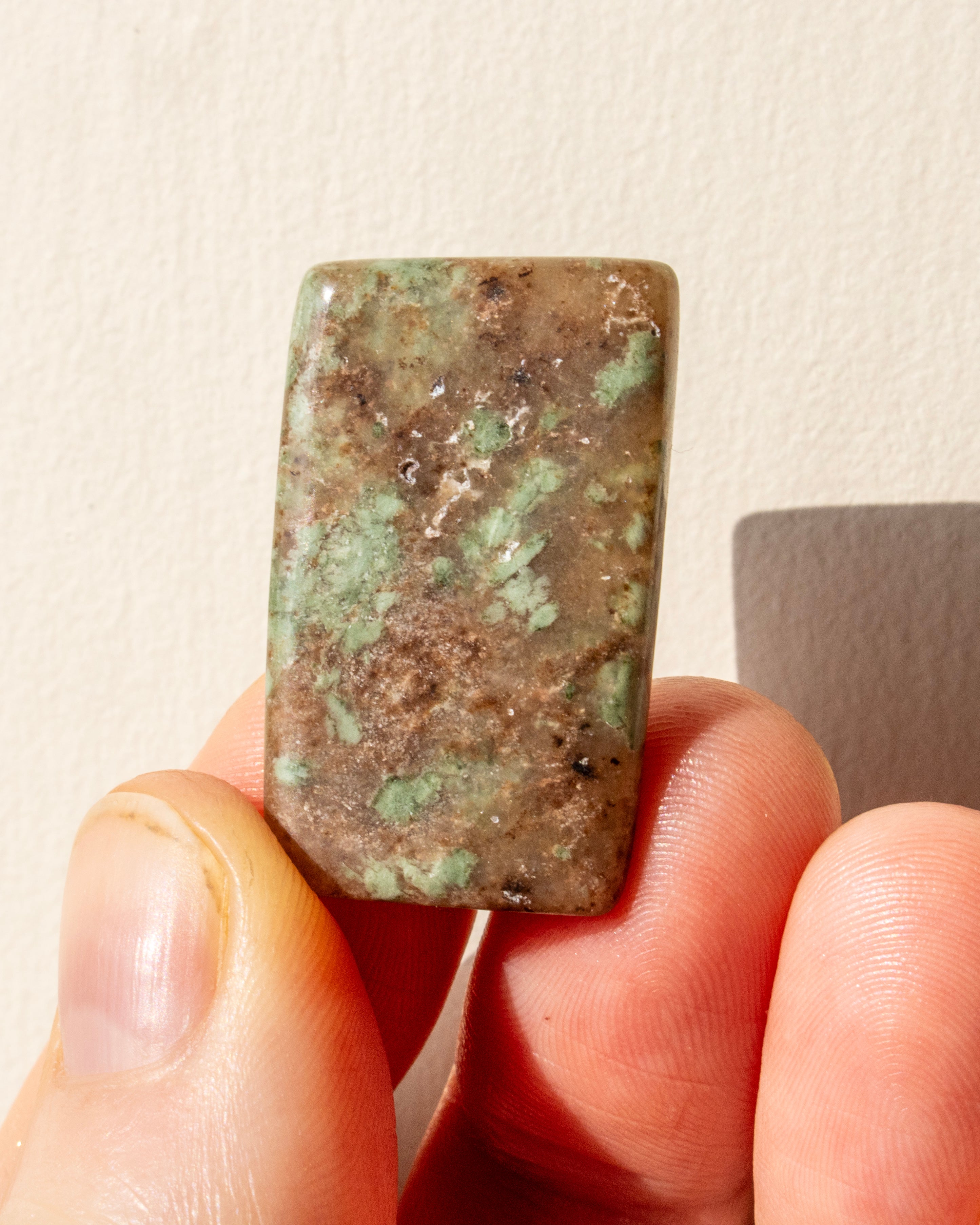 Rectangular green stone held between fingers against a neutral background