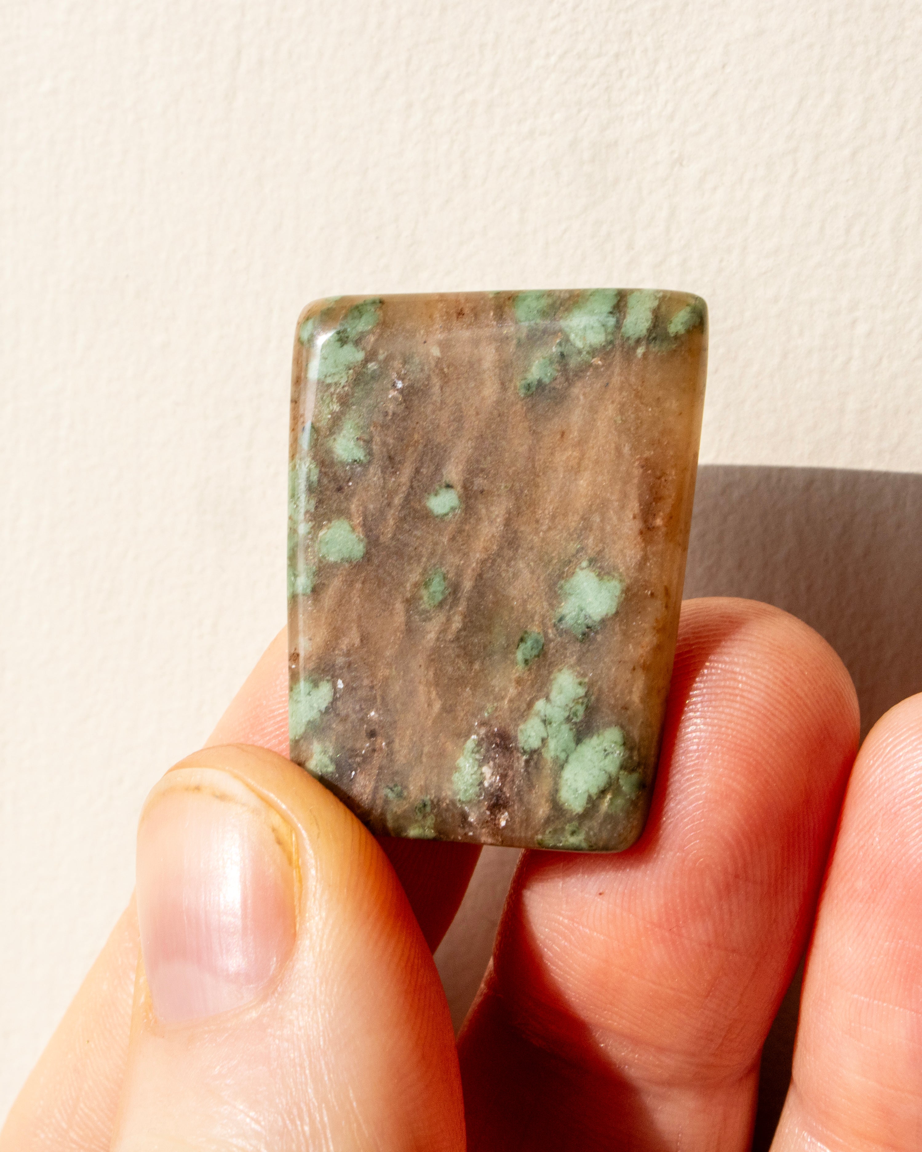 Hand holding a square-shaped green stone against a neutral background