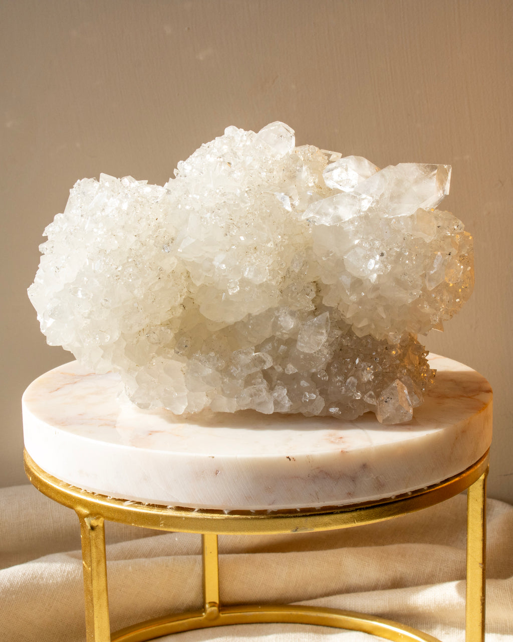 Large crystal formation on a marble and gold stand against a beige background