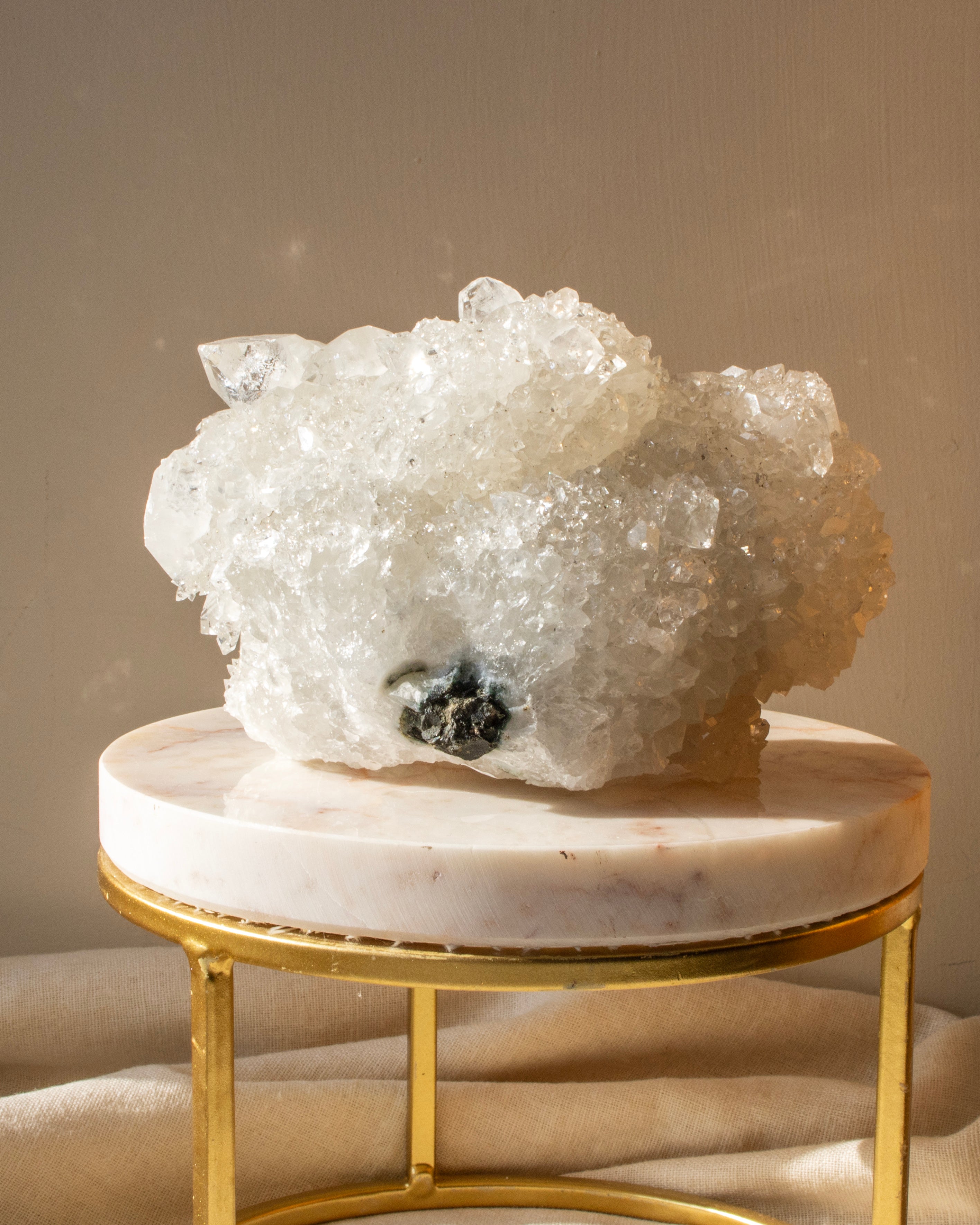 Large crystal formation on a marble and gold stand against a beige background