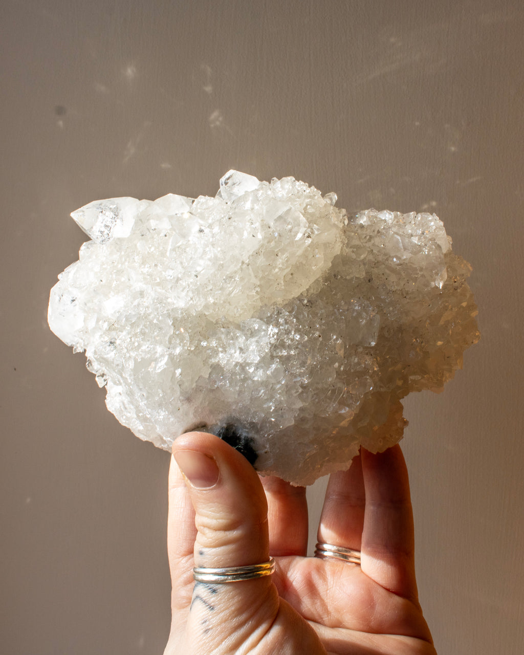Hand holding a large crystal cluster against a neutral background