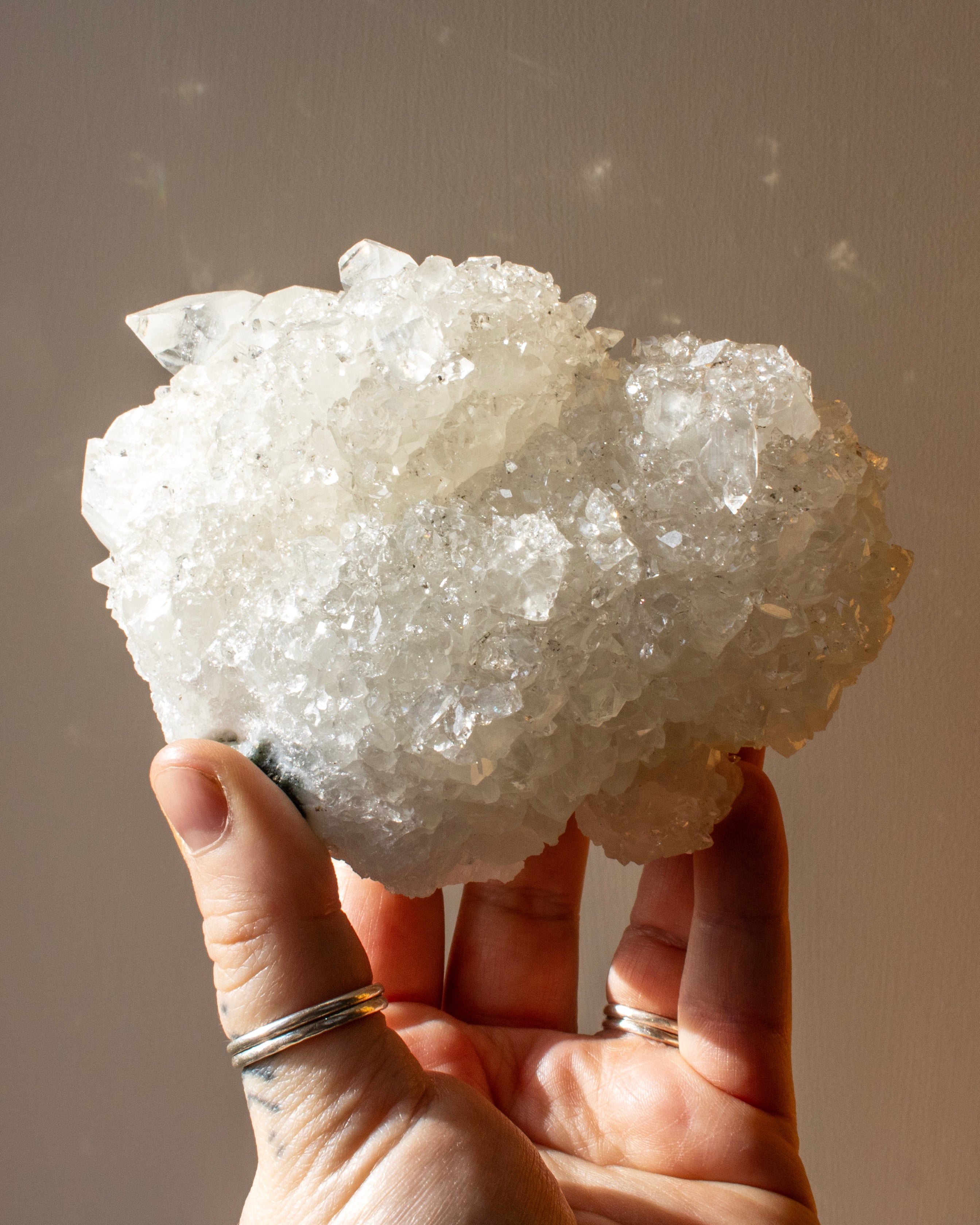 Hand holding a large crystal cluster against a neutral background