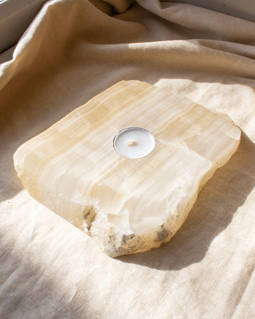 Tealight candle on a rough stone surface with beige fabric background