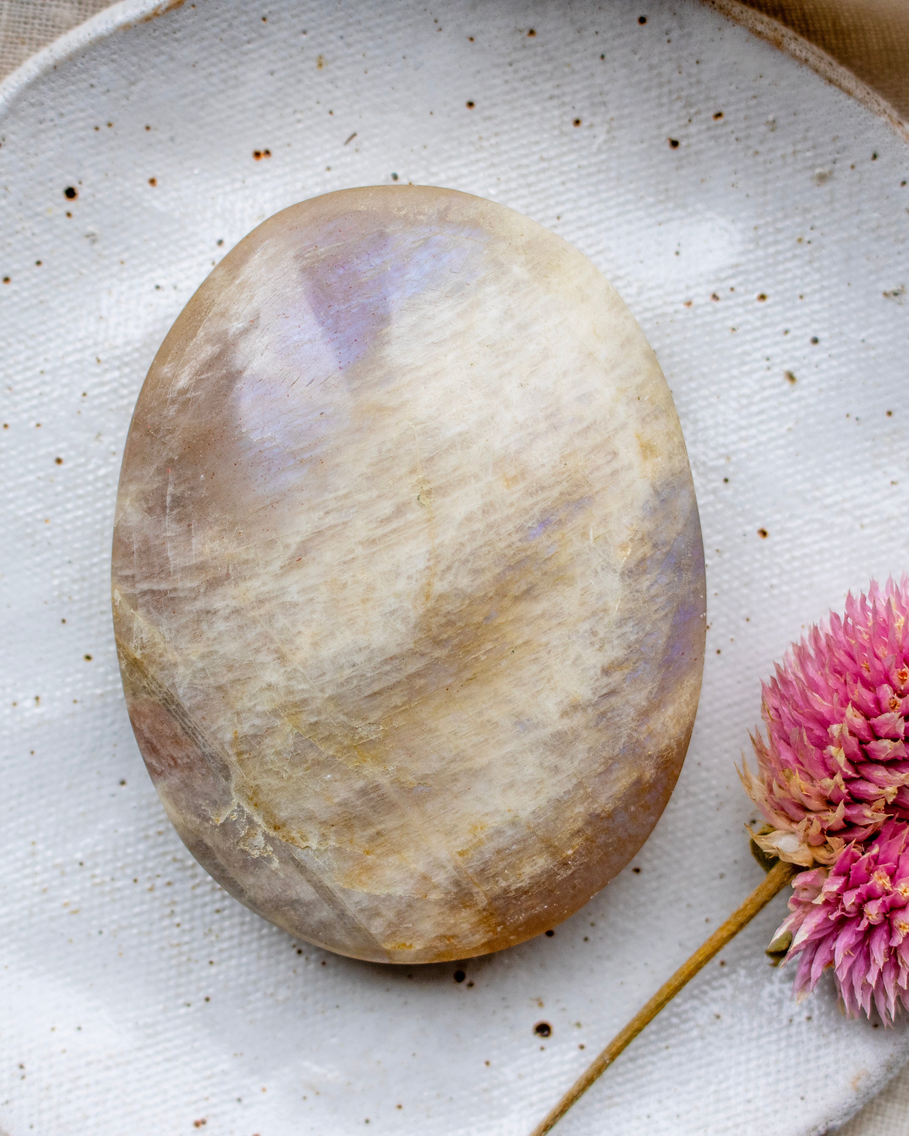 Oval-shaped stone on a textured white surface with a pink flower.