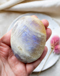 Hand holding a rainbow moonstone crystal with a blurred background