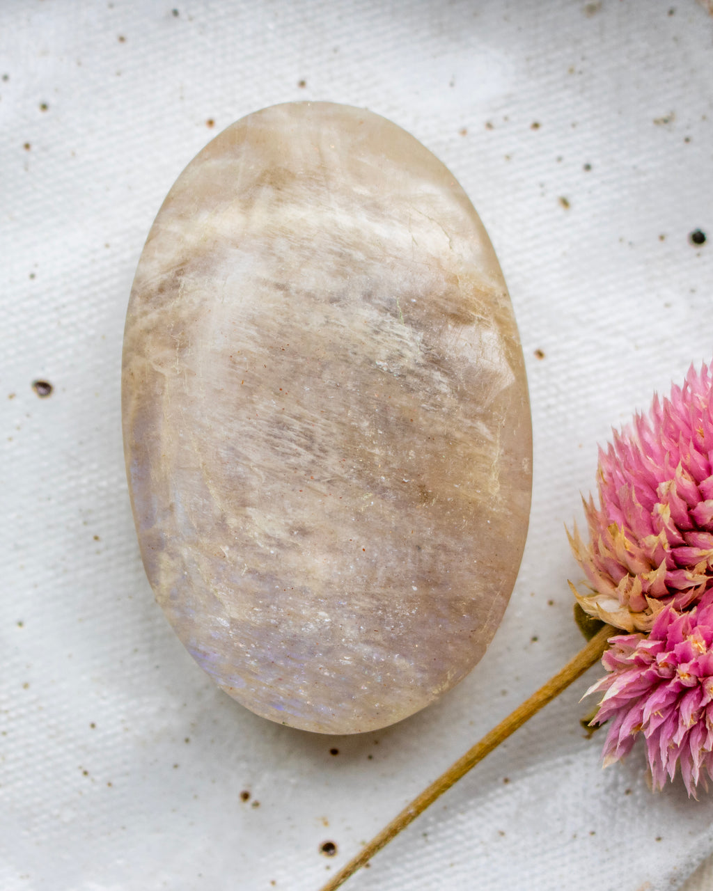Oval-shaped stone on a textured white surface with pink flowers.