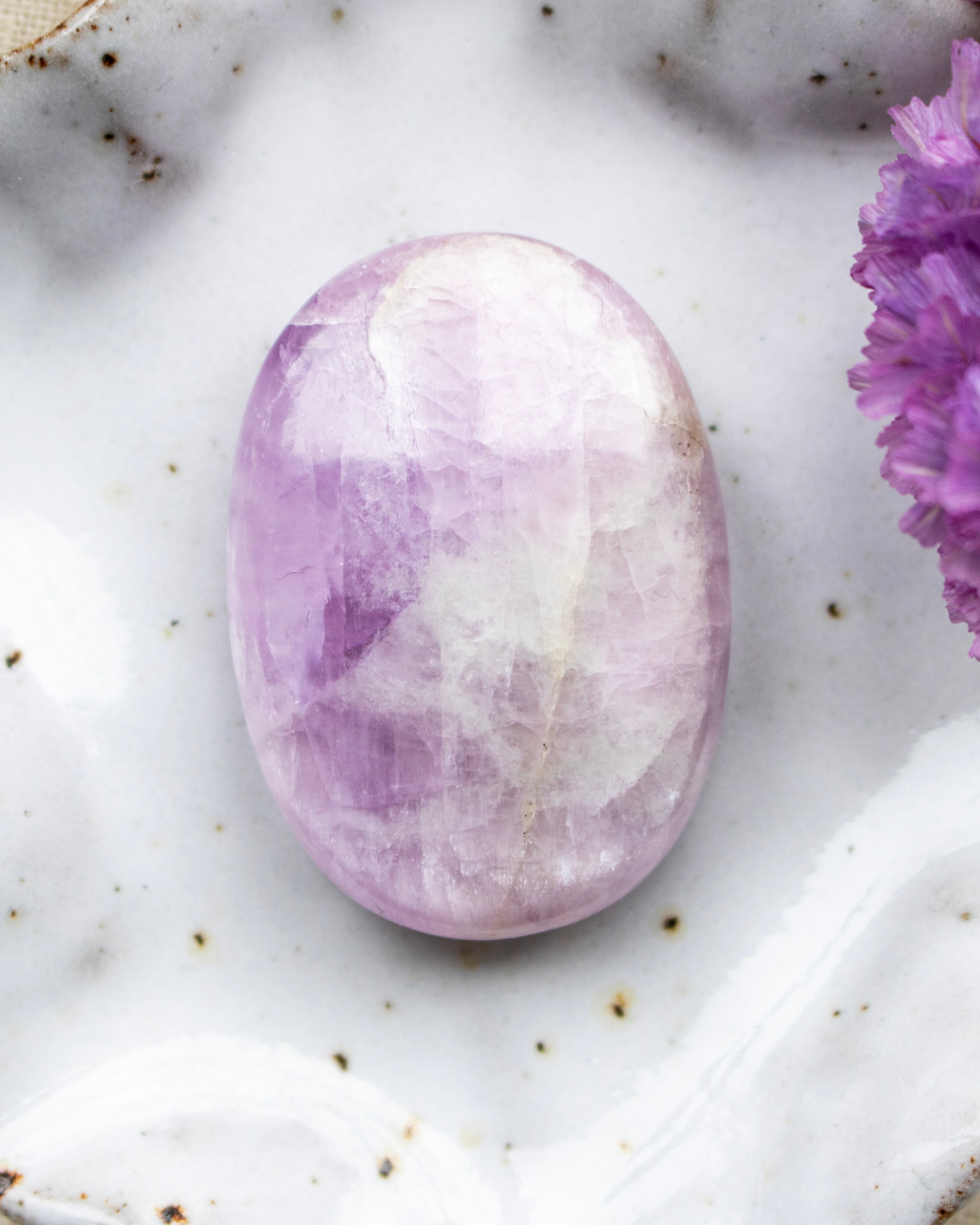 Oval-shaped purple stone on a marble surface with a small purple flower.