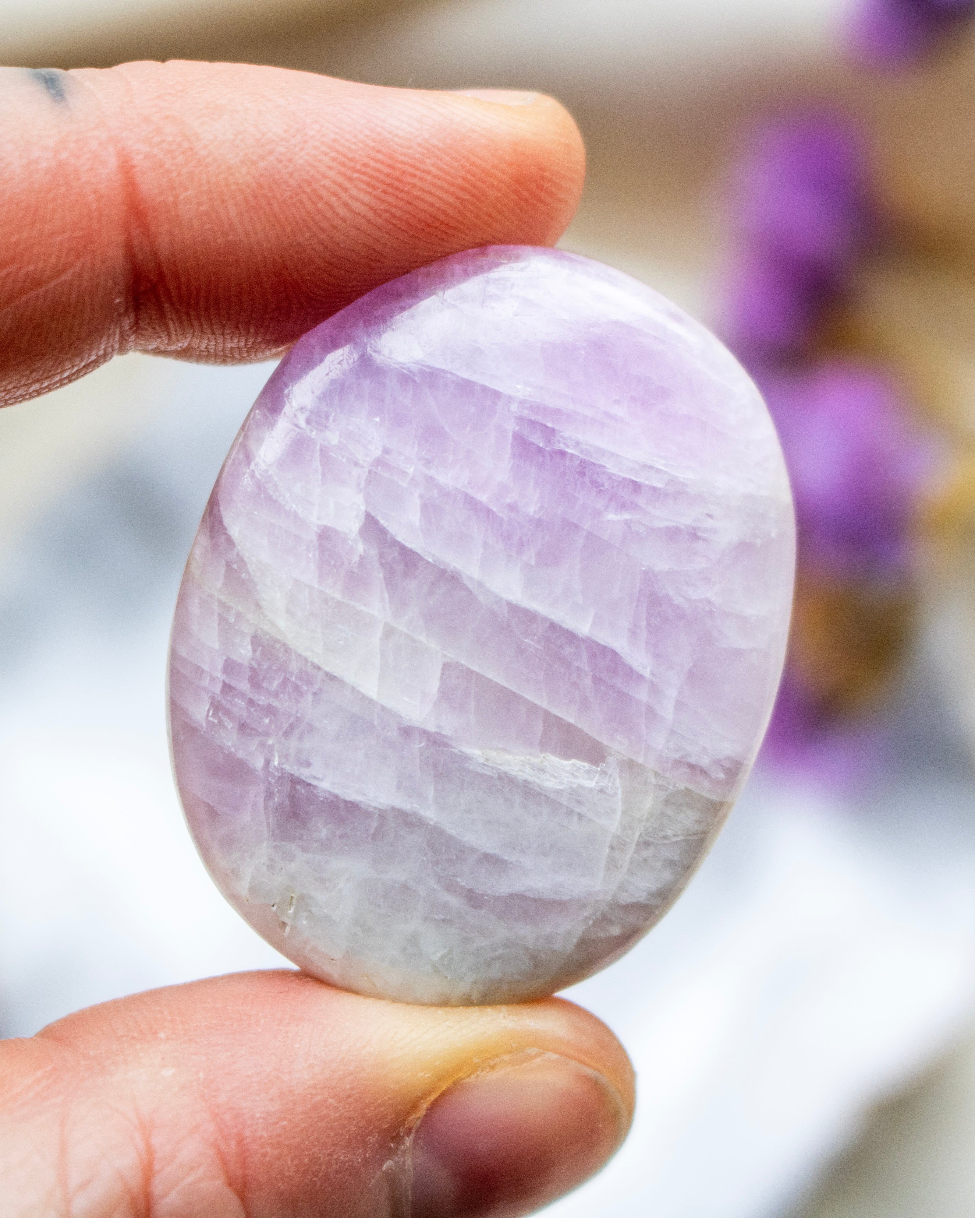 Hand holding a purple and white striped stone with a blurred background